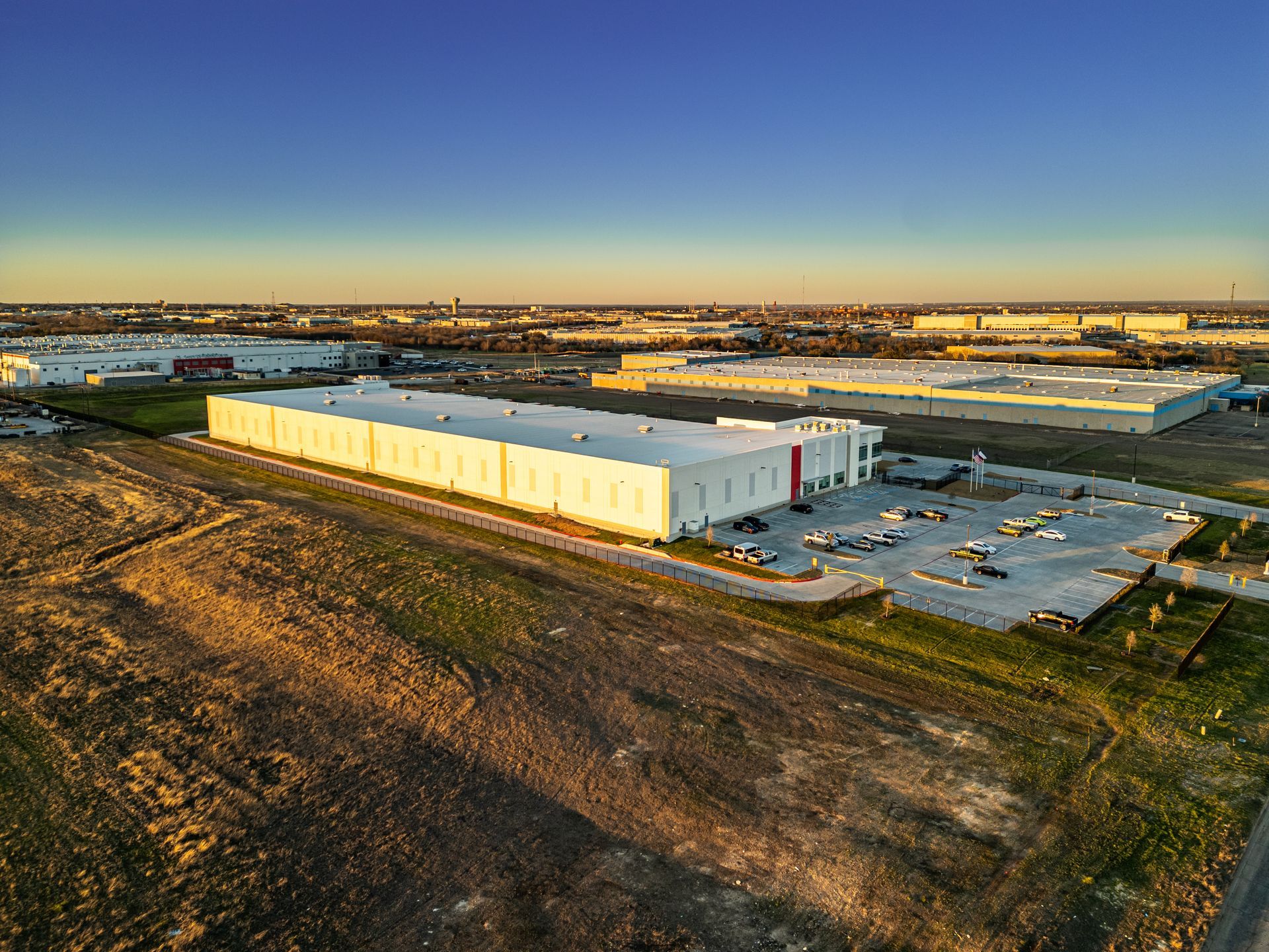 Aerial view of a large, white warehouse in an industrial area at sunset.