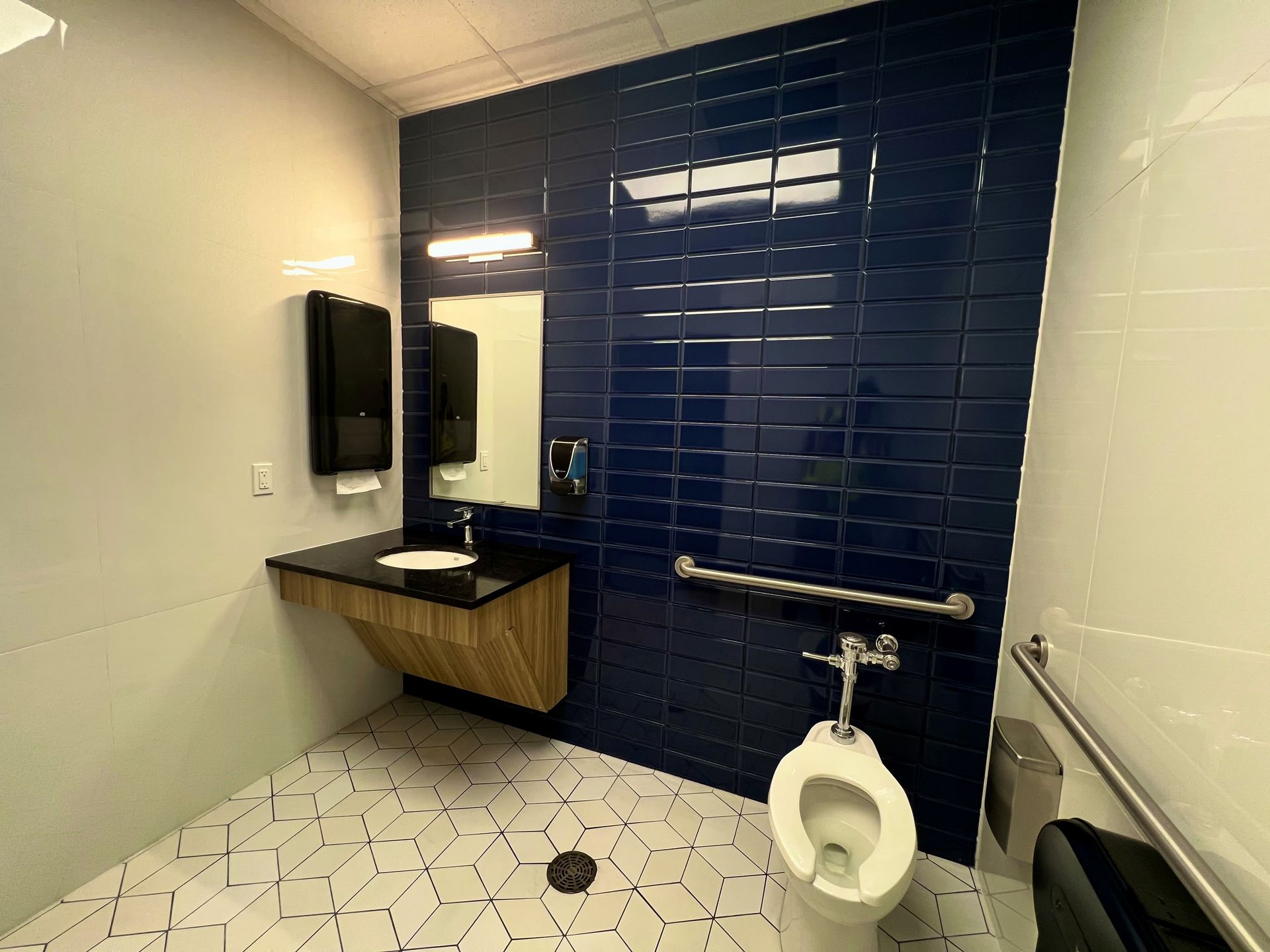 Accessible bathroom with blue tiled accent wall, white fixtures, wood vanity, and grab bar.