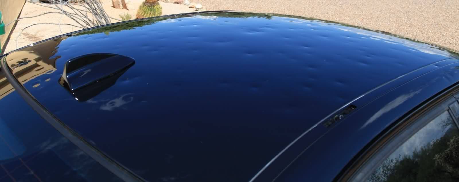 Black car roof with many small dents, likely from hail damage.