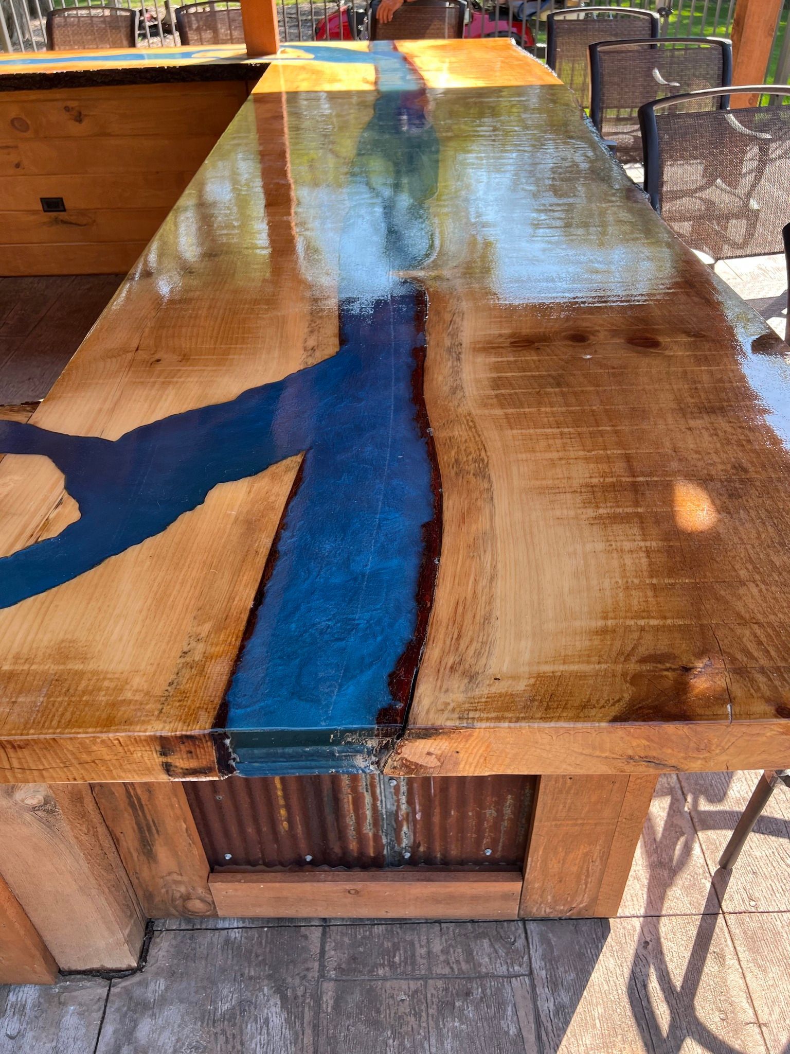 Wooden tabletop with a glossy blue resin river running through the center in a patio setting