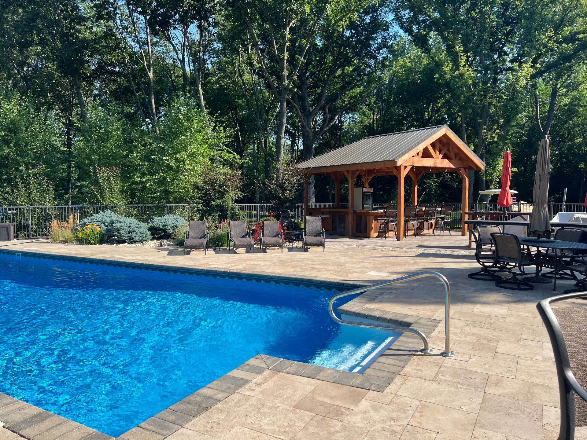 Backyard pool with blue water, stone deck, and a wooden gazebo with seating in the background