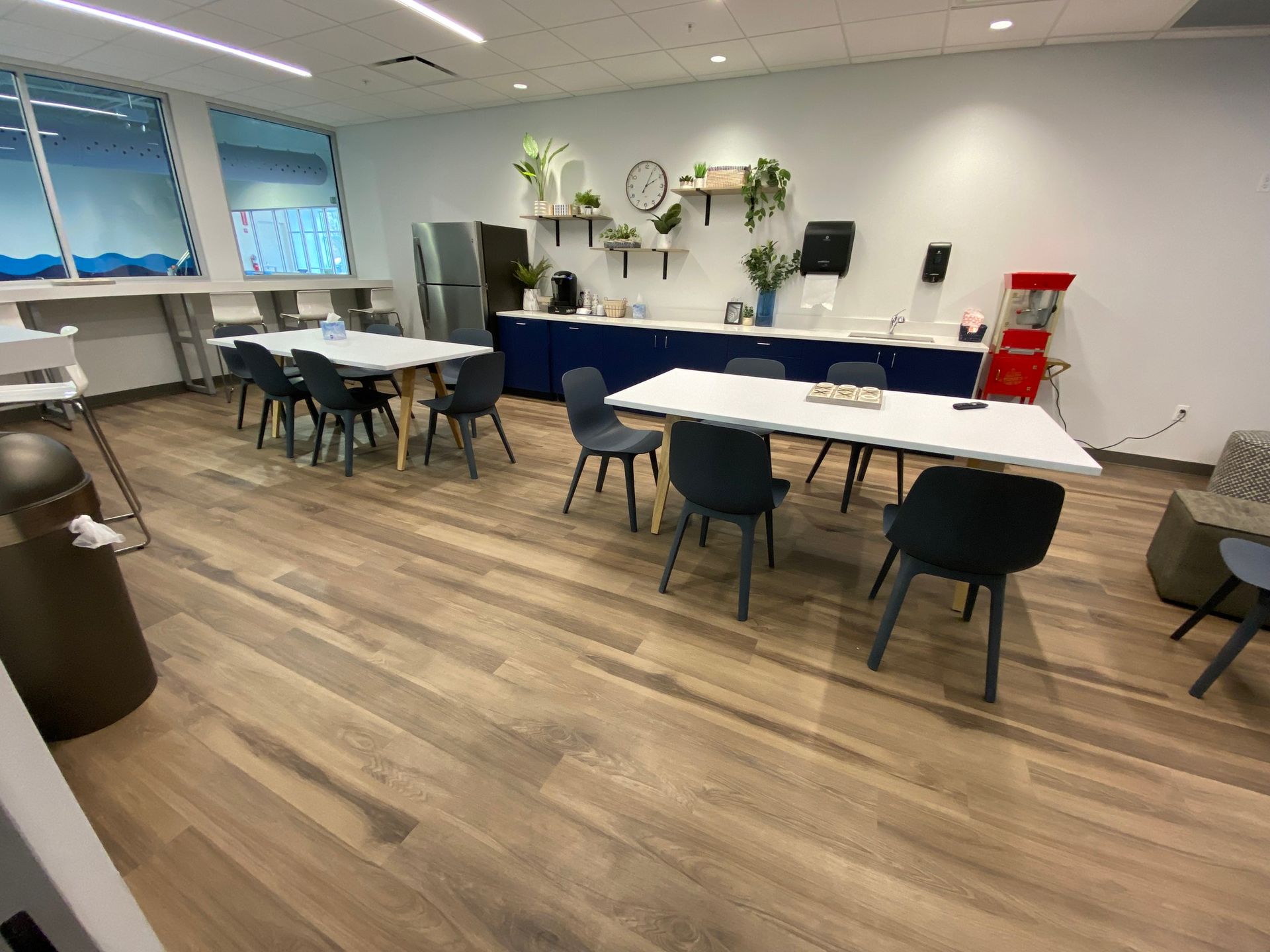 Quiet break room with tables, chairs, couches, and a counter against white walls.