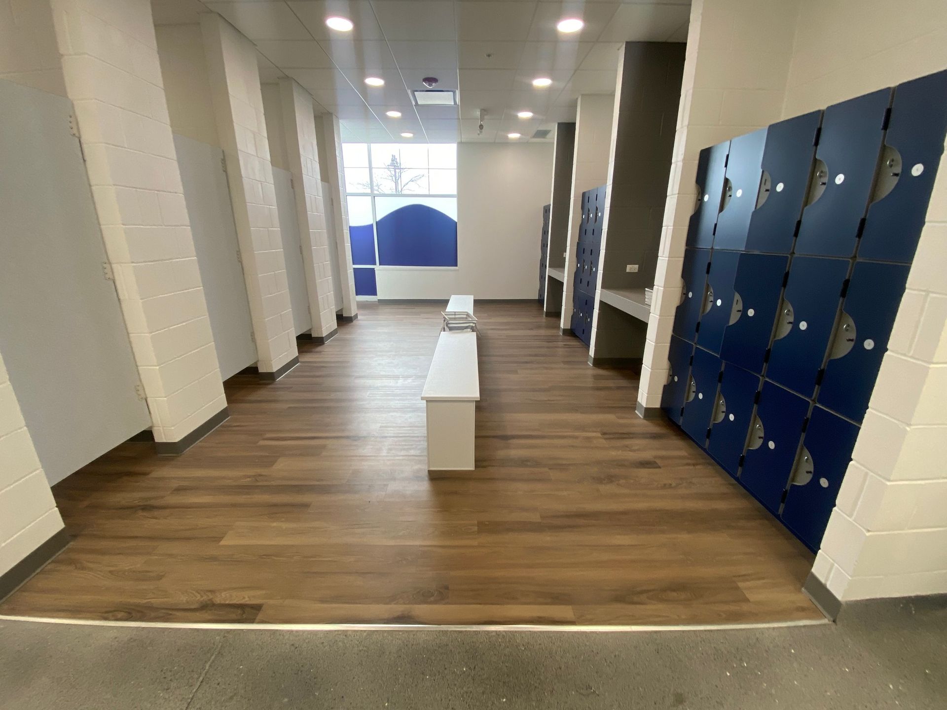 Empty hallway with blue lockers, white benches, and wood flooring in a modern school or office interior