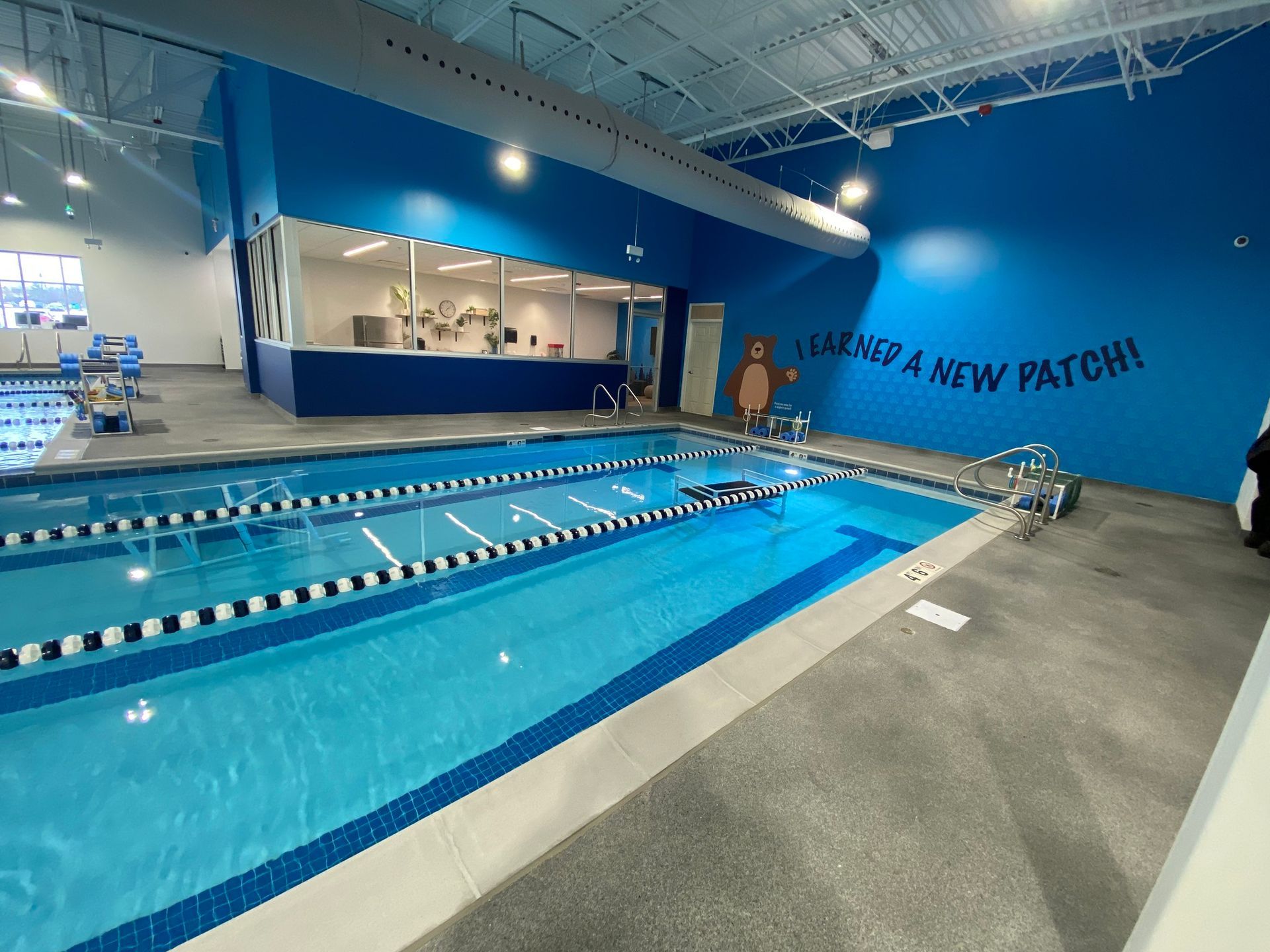 Indoor lap pool with blue water, lane dividers, and a covered spectator area in a bright gym facility