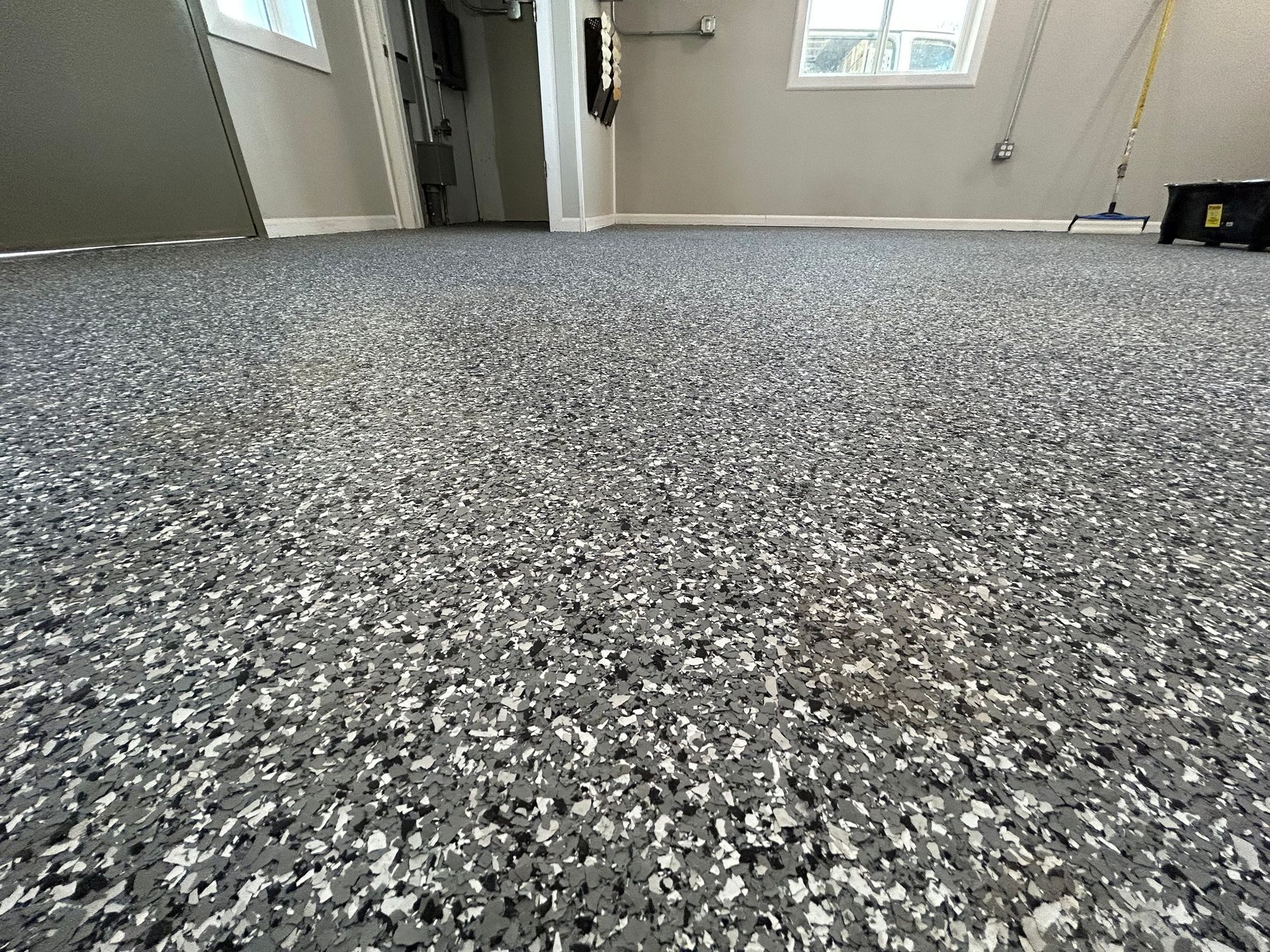 Low-angle view of a speckled gray carpet in an empty room with windows and an open doorway