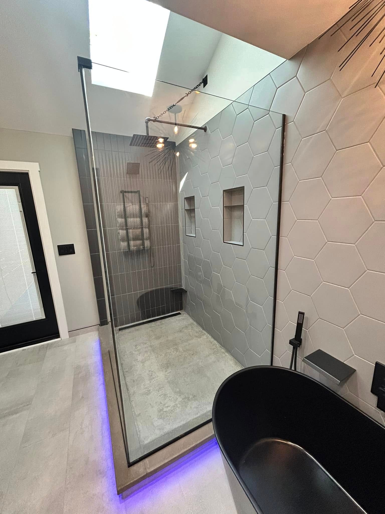 Modern bathroom with glass shower enclosure, hexagon tile wall, and purple LED floor lighting