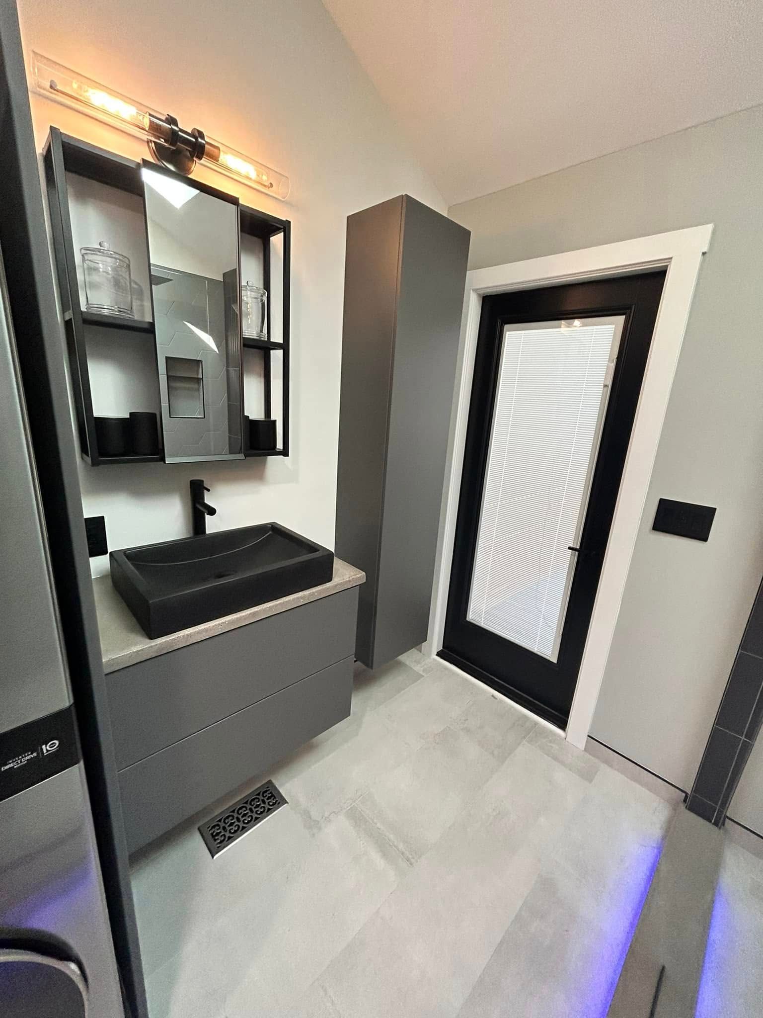 Modern bathroom with black vanity, mirror cabinet, glass shower door, and gray tile flooring