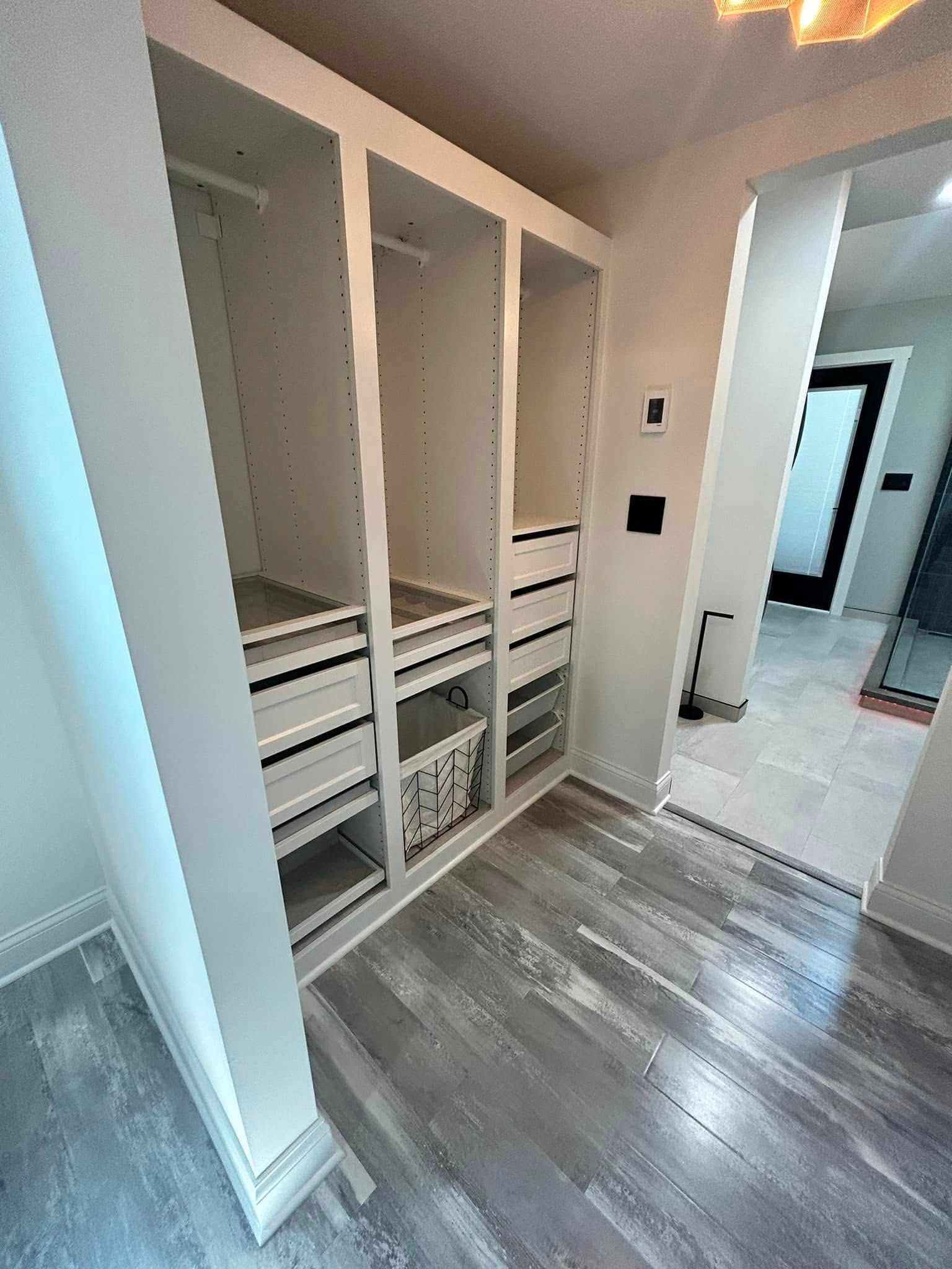 Empty walk-in closet with white shelving and gray wood flooring, viewed from the doorway.