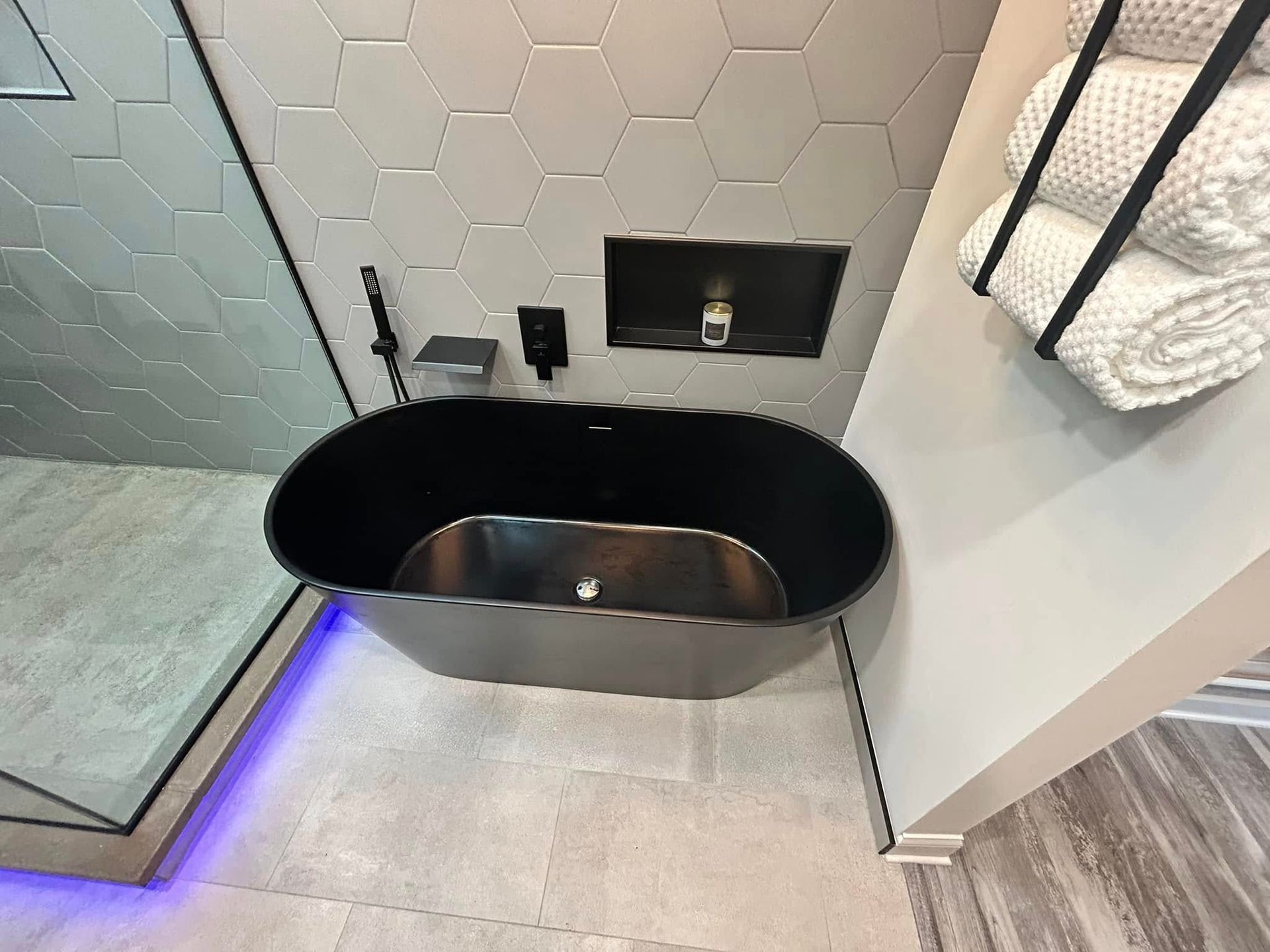 Modern black soaking tub in a tiled bathroom with blue accent lighting