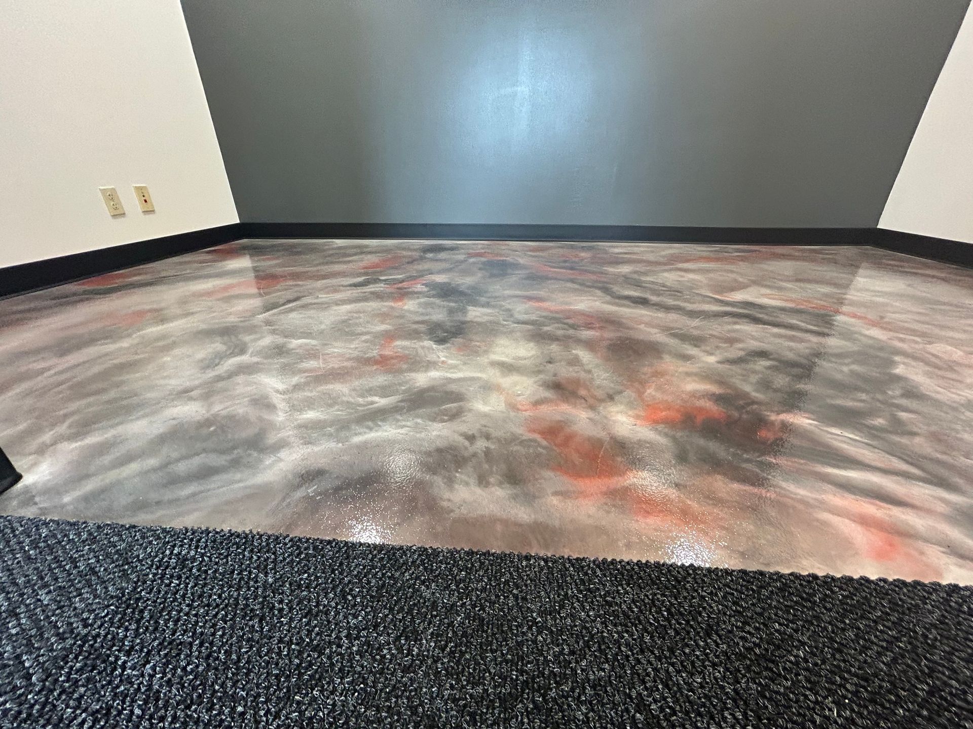 Empty room with gray walls and dark carpet, featuring a marbled gray, white, and red floor section.