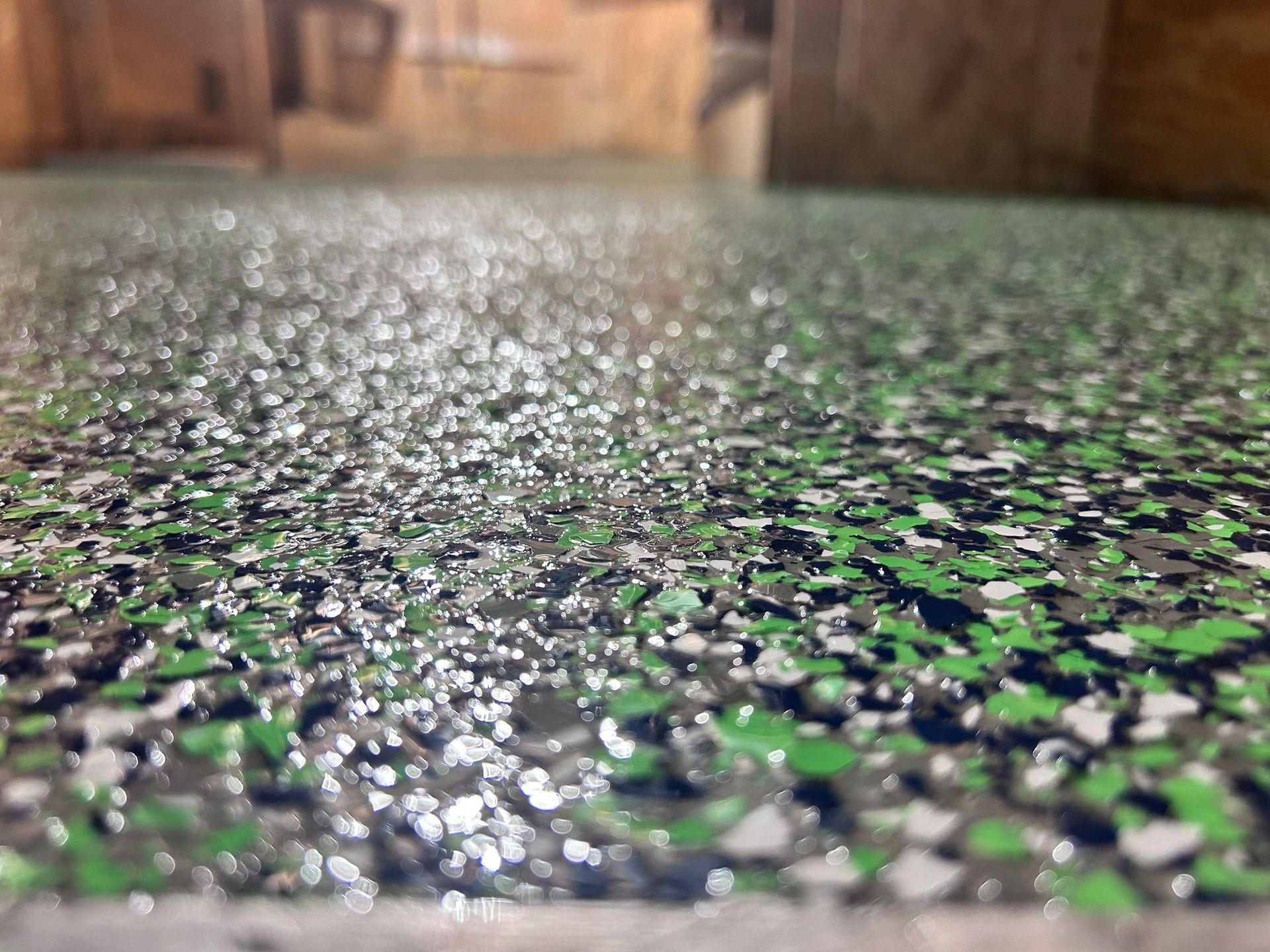 Close-up of a wet, speckled green and black countertop with blurred wood cabinets in the background