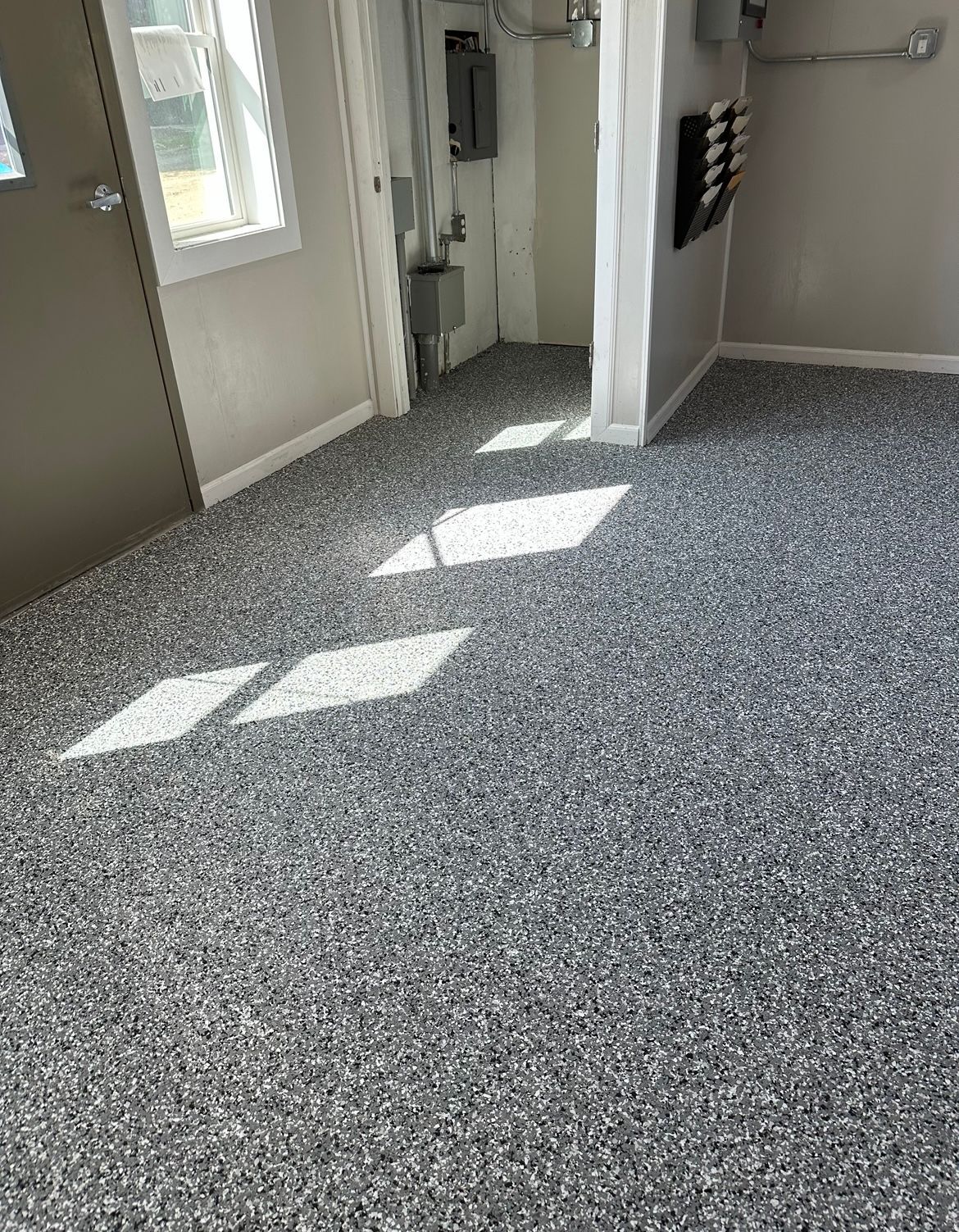 Sunlit empty room with speckled gray carpet, white walls, and a door to the outside.