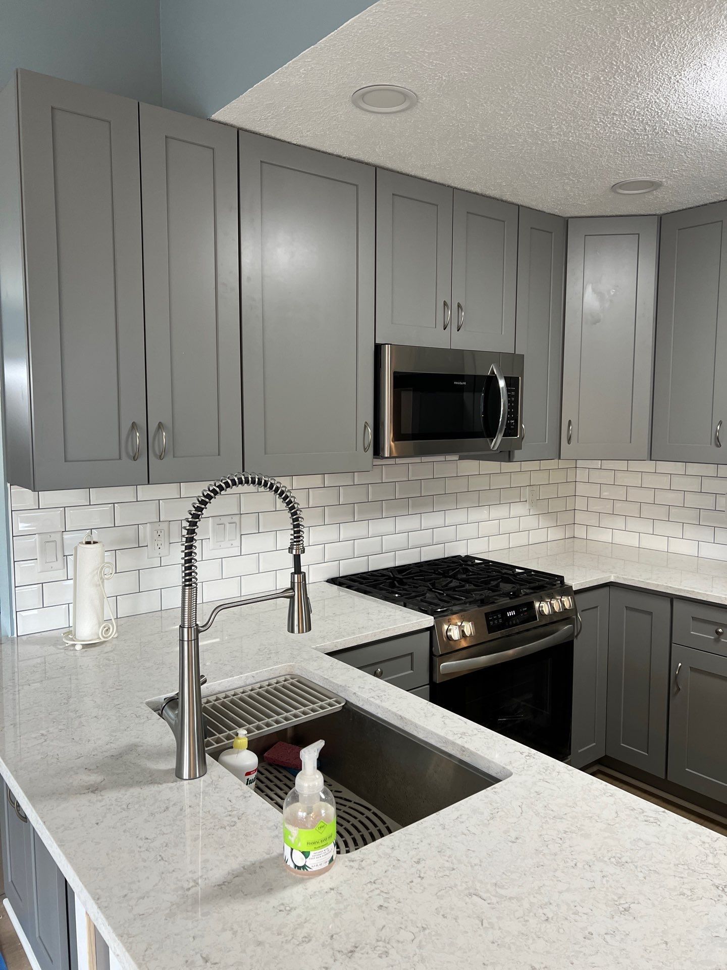Modern kitchen with gray cabinets, stainless appliances, white backsplash, and sink island