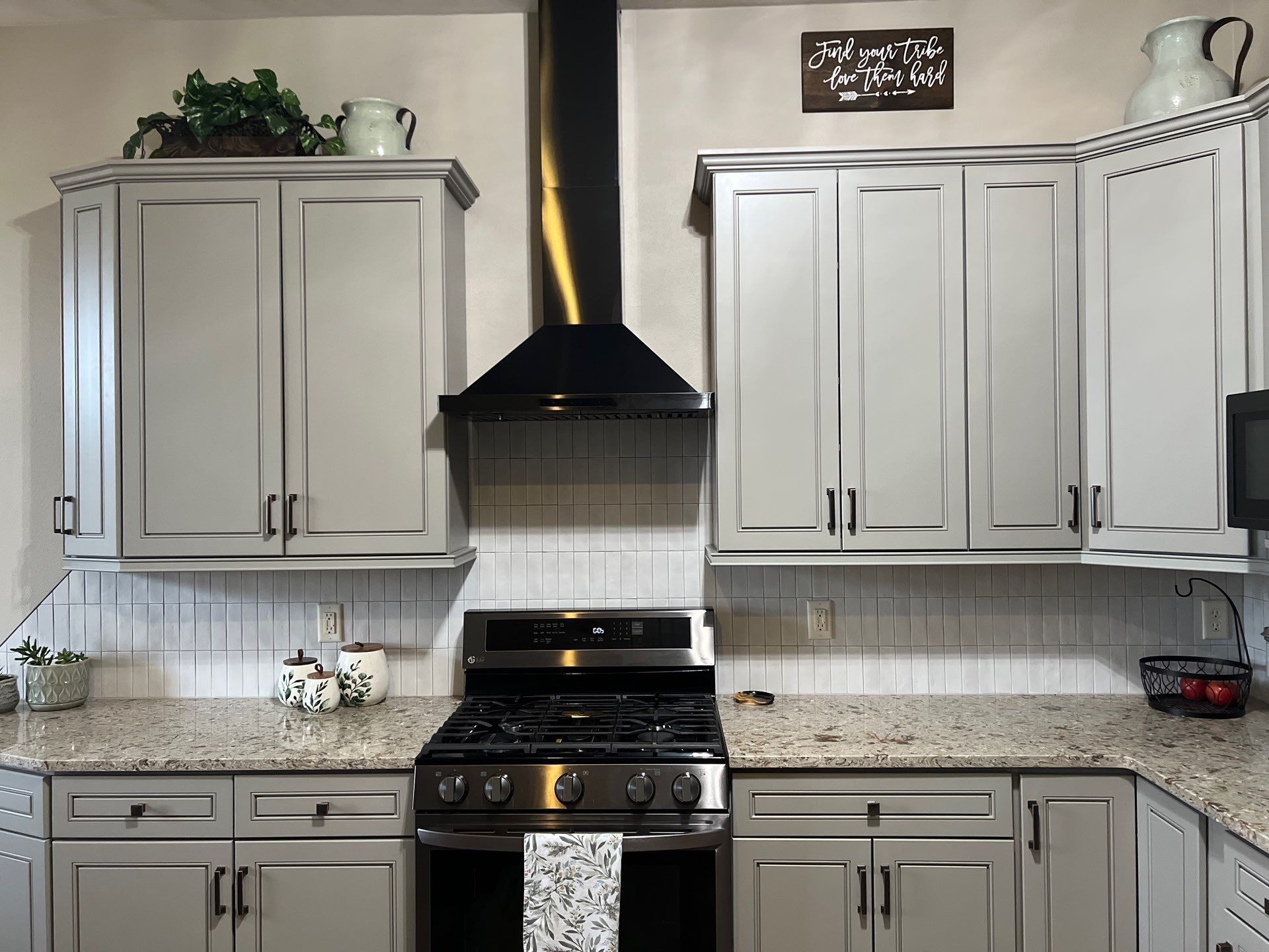 Modern kitchen with gray cabinets, black range hood, granite countertops, and stainless steel stove.