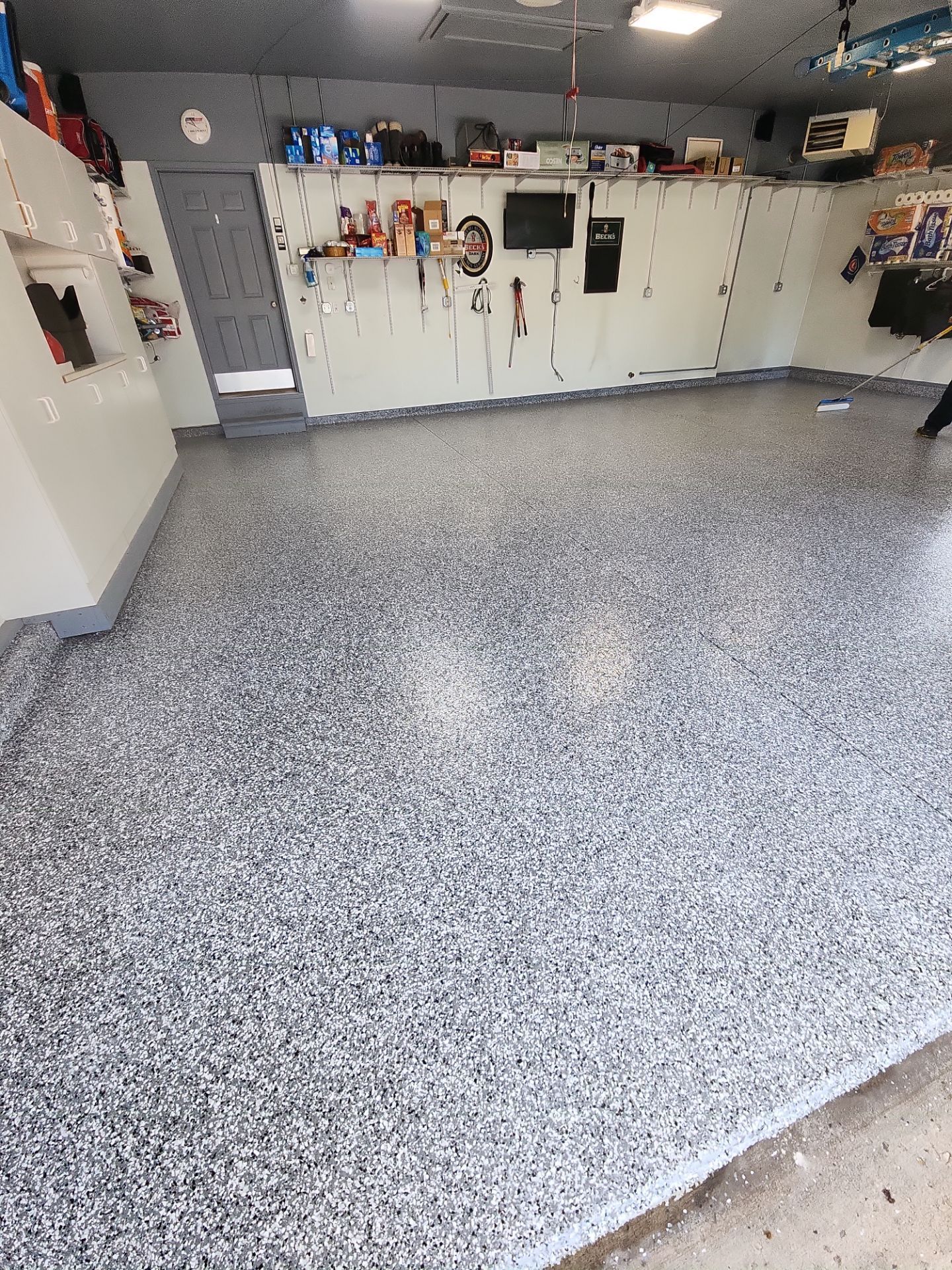 Spacious garage with gray speckled epoxy floor and white cabinets along the back wall.