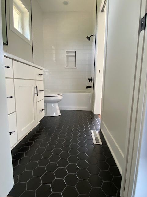 Narrow bathroom with black hex tile floor, white vanity, toilet, and bathtub