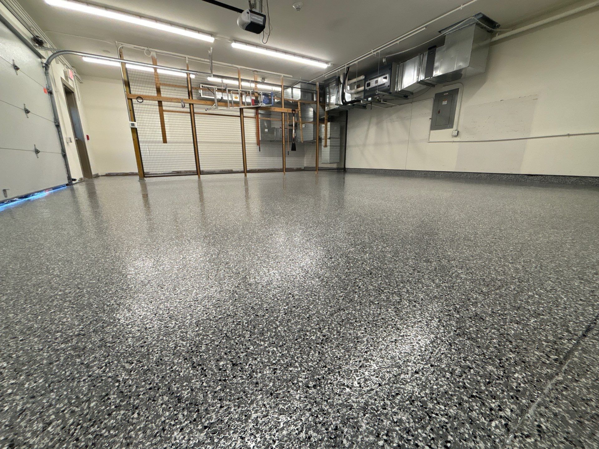 Empty indoor garage with a speckled epoxy floor, white walls, overhead lights, and windows along the back wall