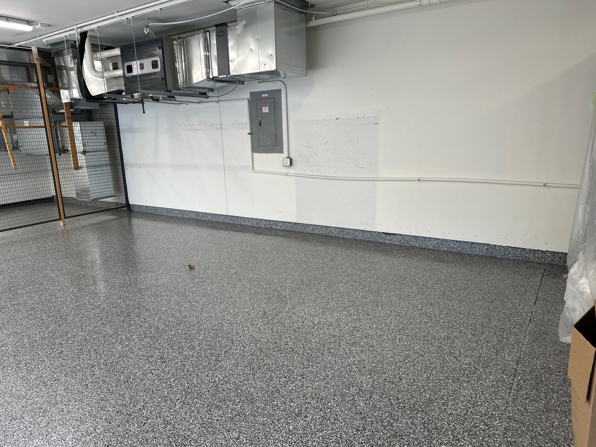 Empty industrial room with gray speckled floor, white walls, exposed ductwork, and electrical panels