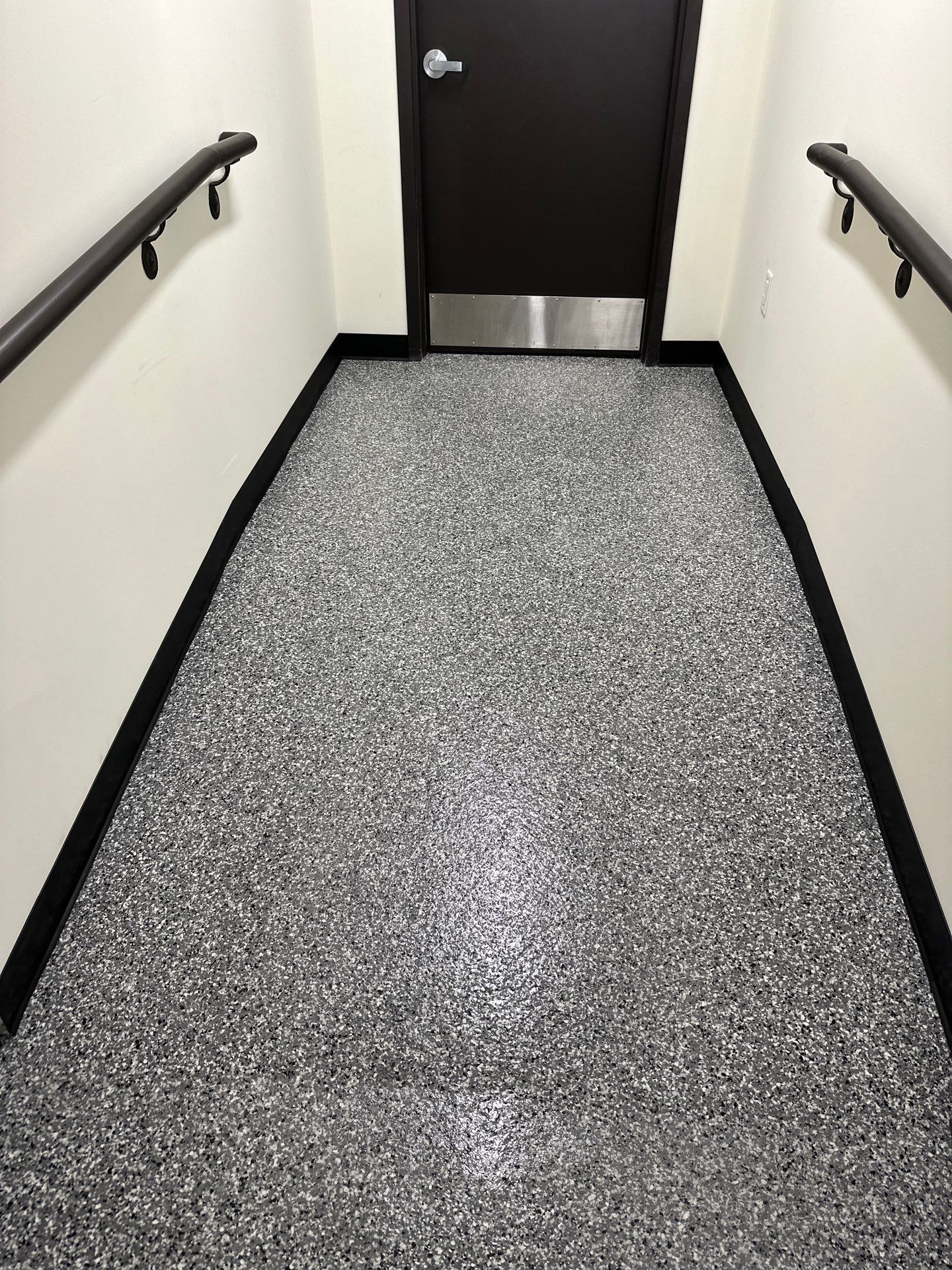 Narrow carpeted hallway with black handrails leading to a closed black door.