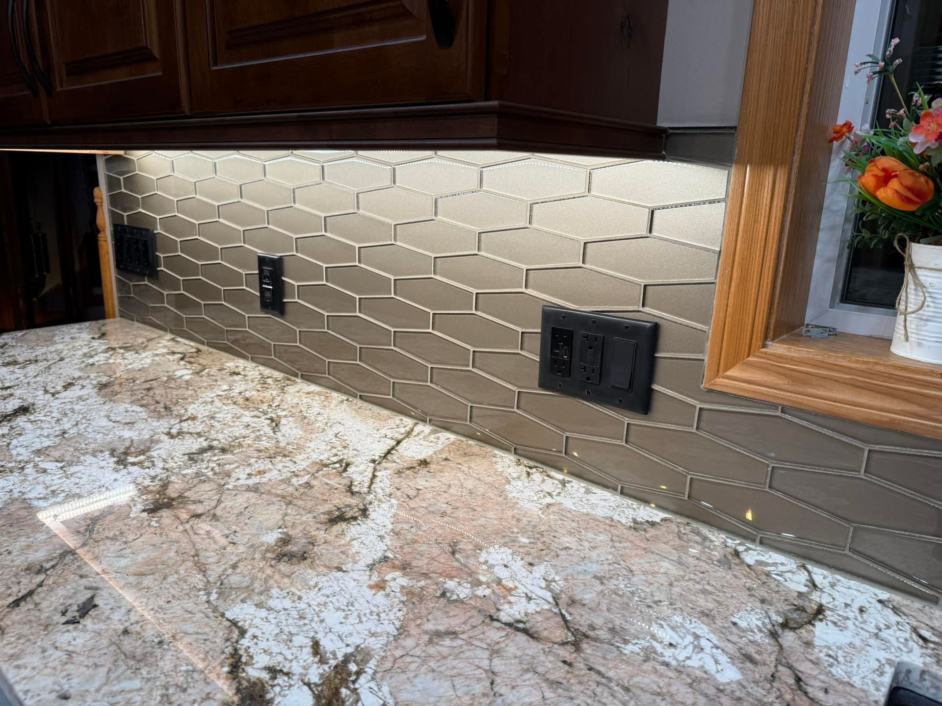 Kitchen backsplash with tan hex tiles, under-cabinet lighting, outlets, and granite countertop edge