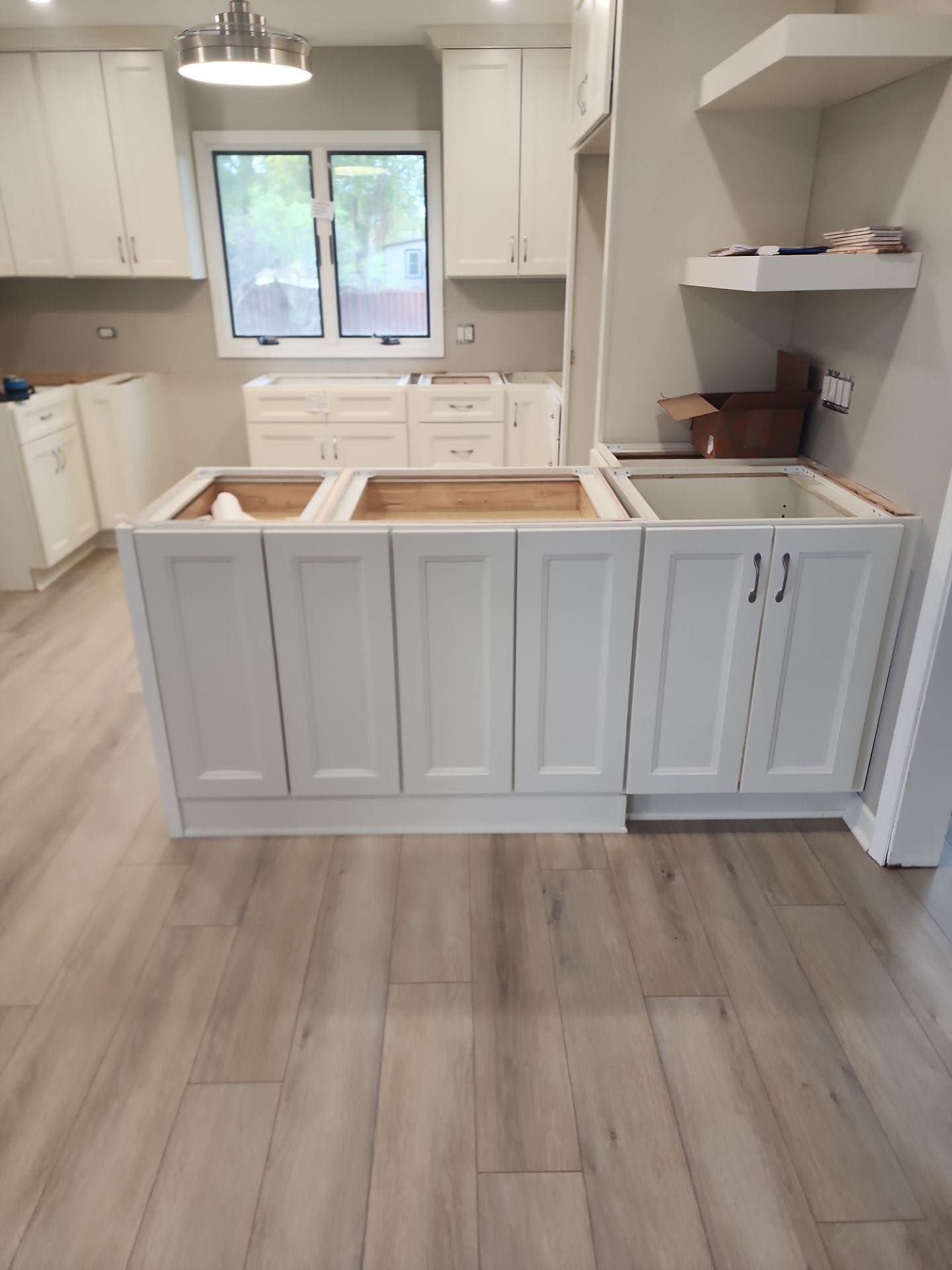Bright kitchen with white cabinets, gray island, wood floor, and a window over the sink.