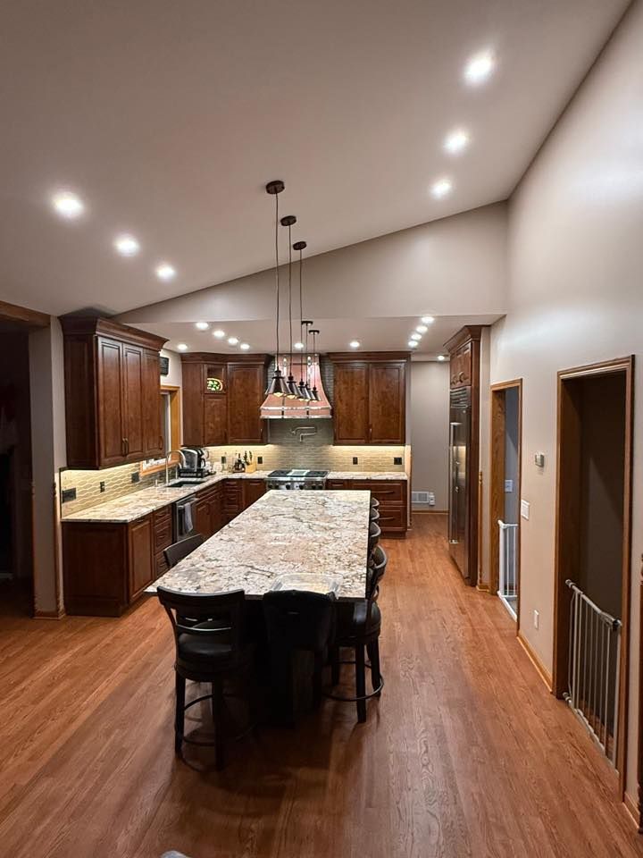 Modern kitchen with a large granite island, dark wood cabinets, pendant lights, and hardwood floors