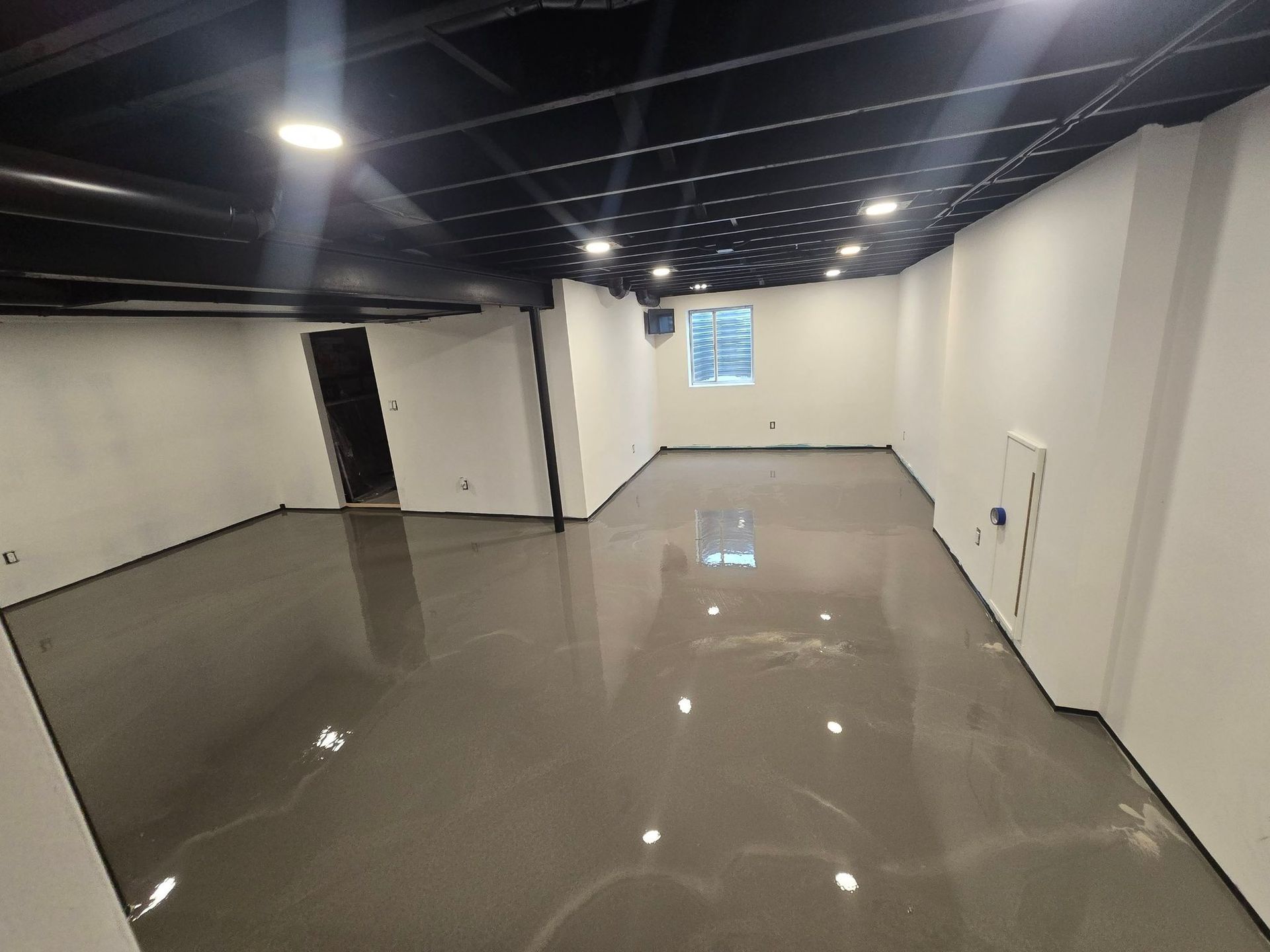 Empty modern room with glossy gray floor, white walls, and exposed black ceiling lights