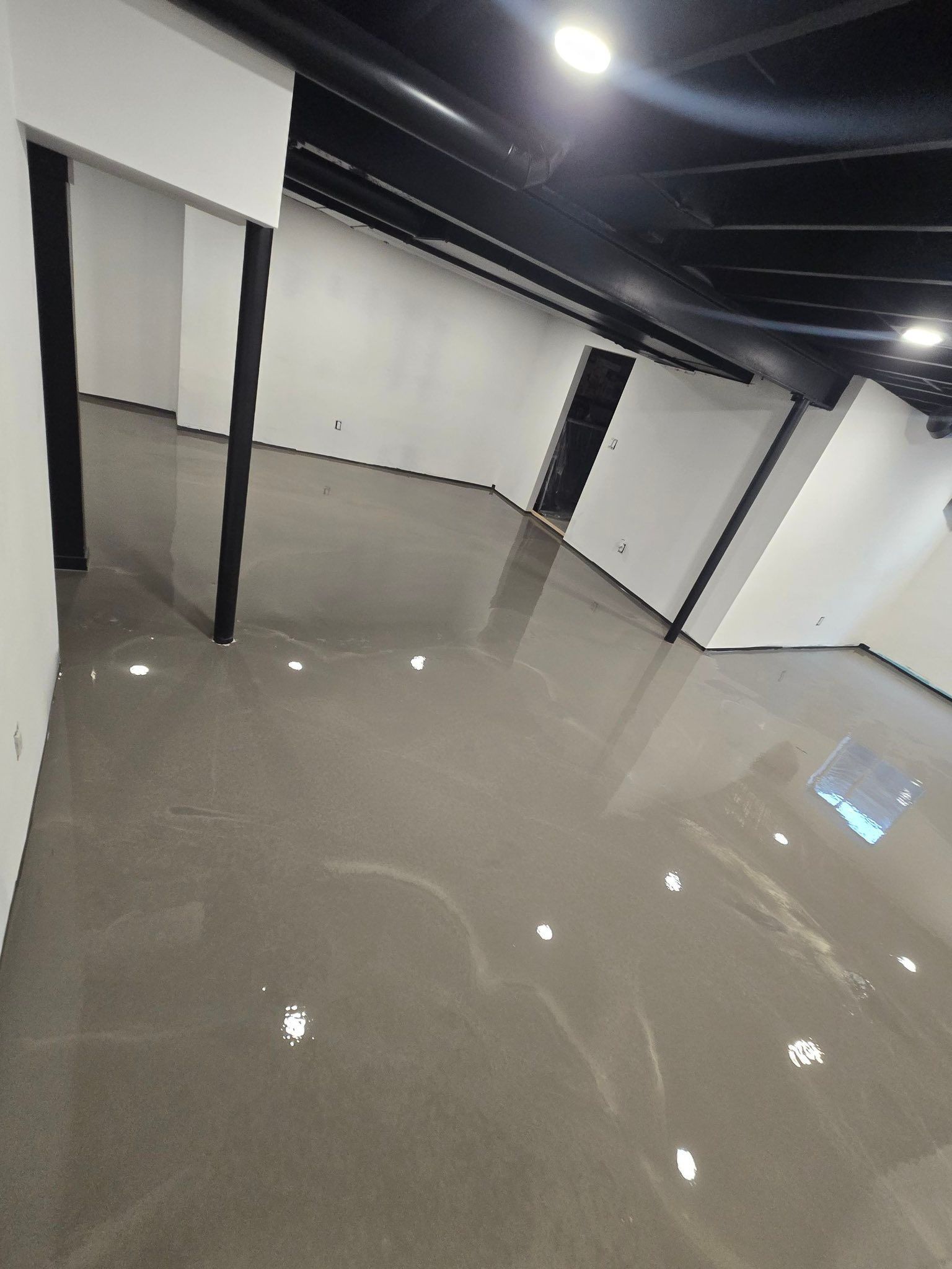 Empty indoor room with glossy gray floor, white walls, and black ceiling beams