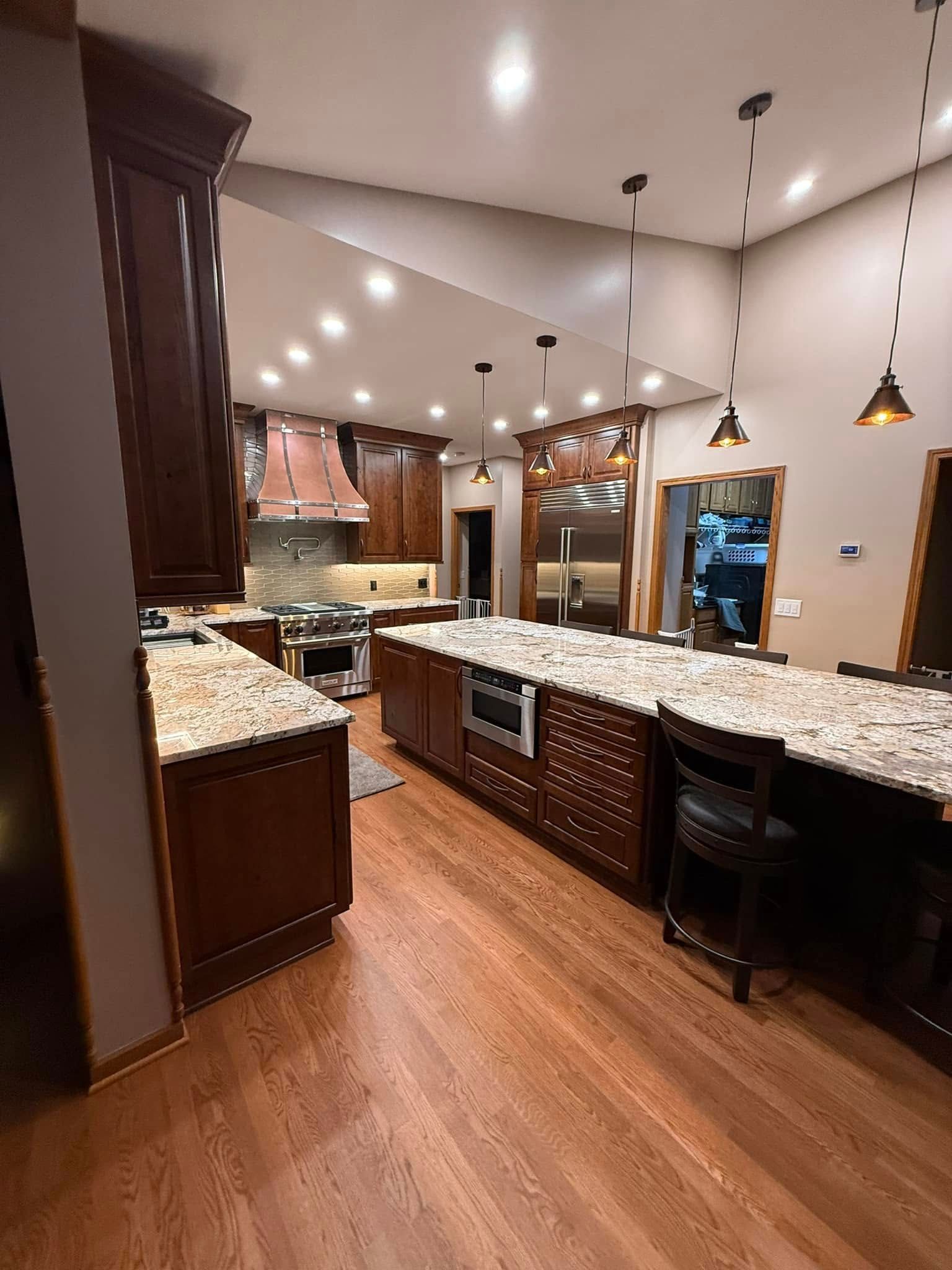 Open-concept kitchen with dark wood cabinets, granite island, pendant lights, and hardwood floors
