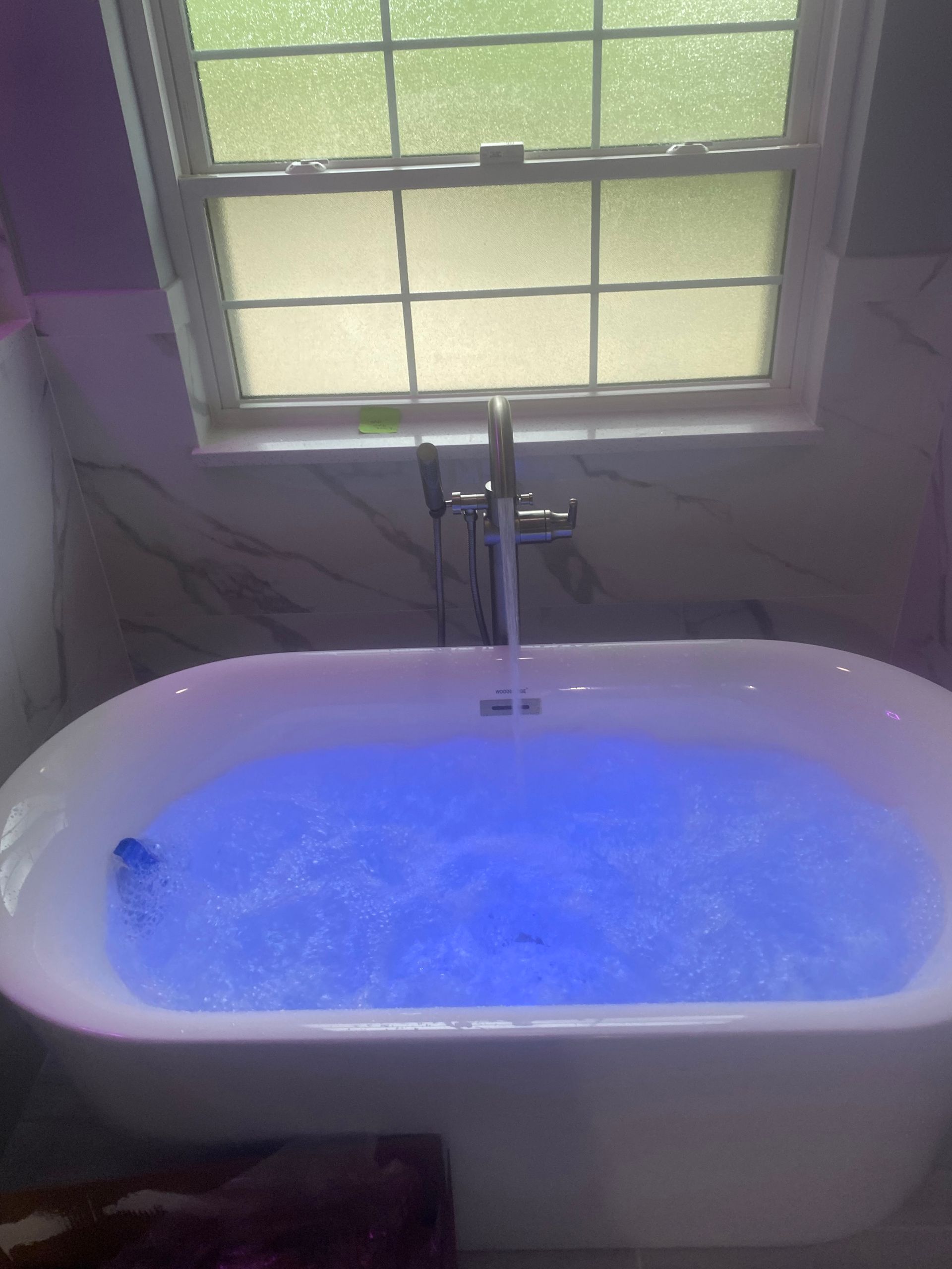 A bathtub with blue water in it is in a bathroom next to a window.