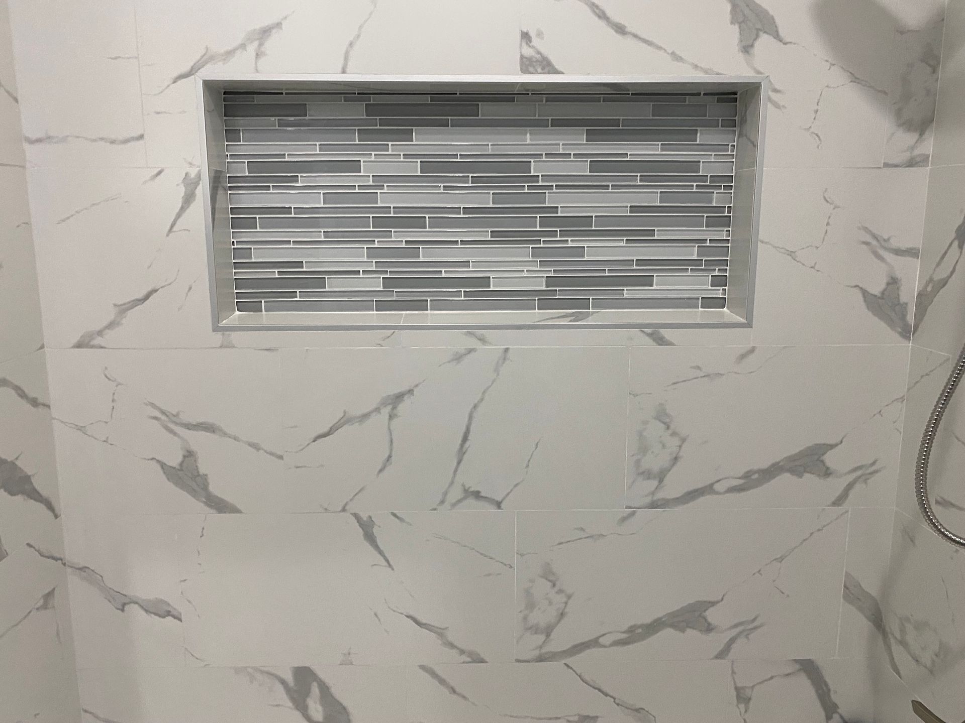 A shower niche in a bathroom with marble tiles and a shower head.