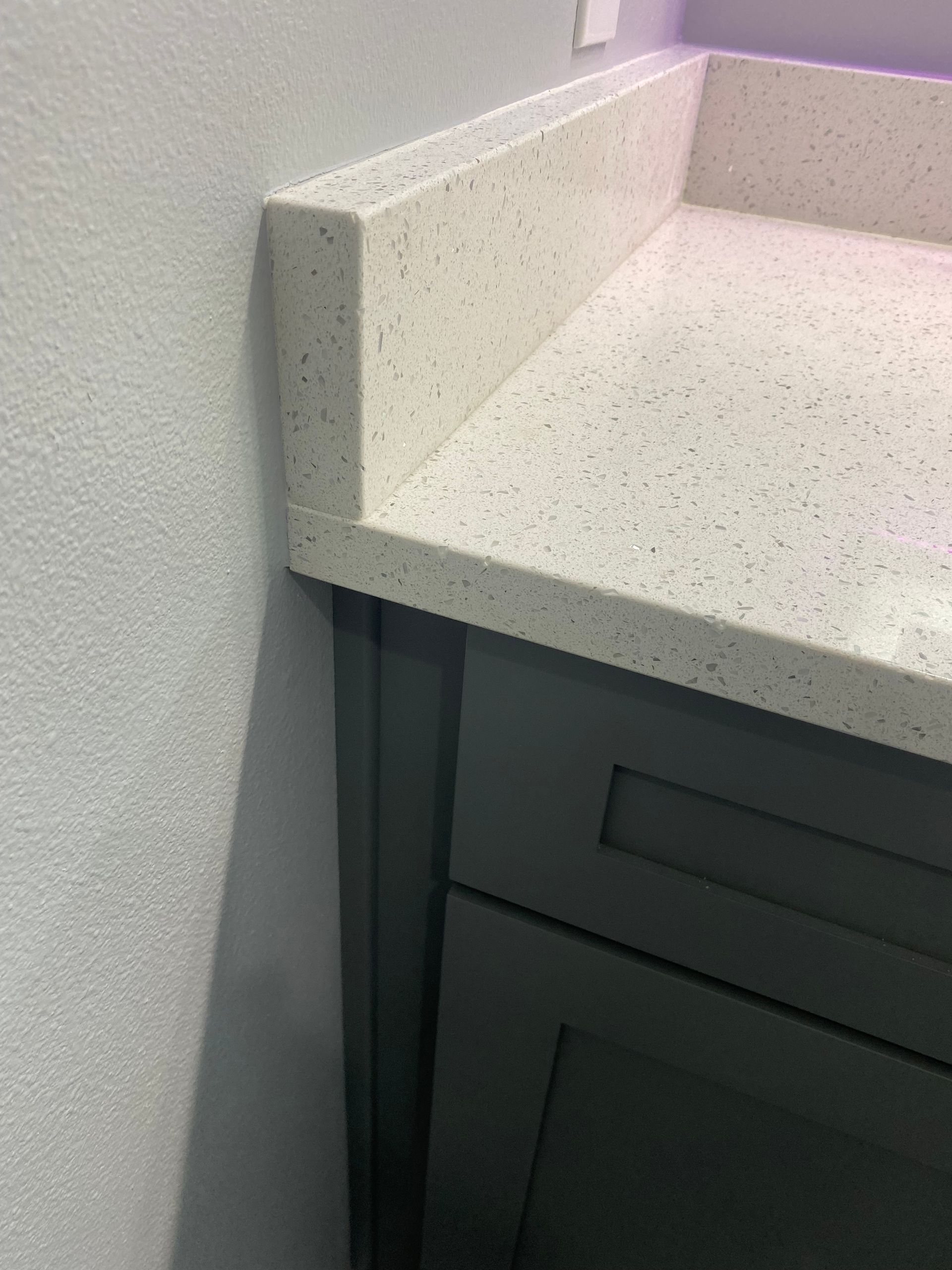A bathroom vanity with a white counter top and gray cabinets.