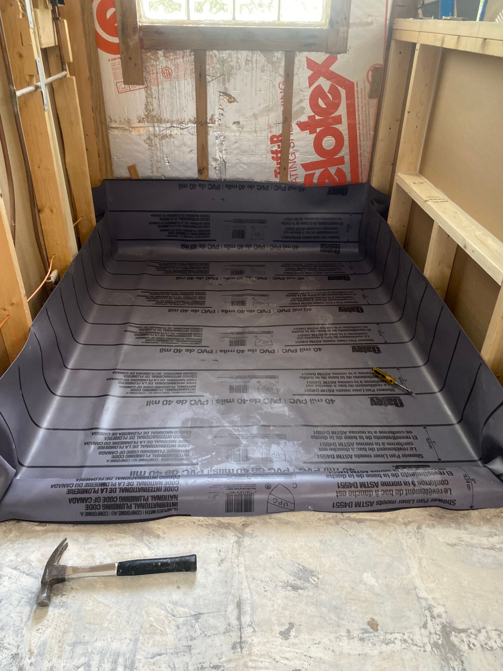 A hammer is sitting on the floor next to a sheet of foam.