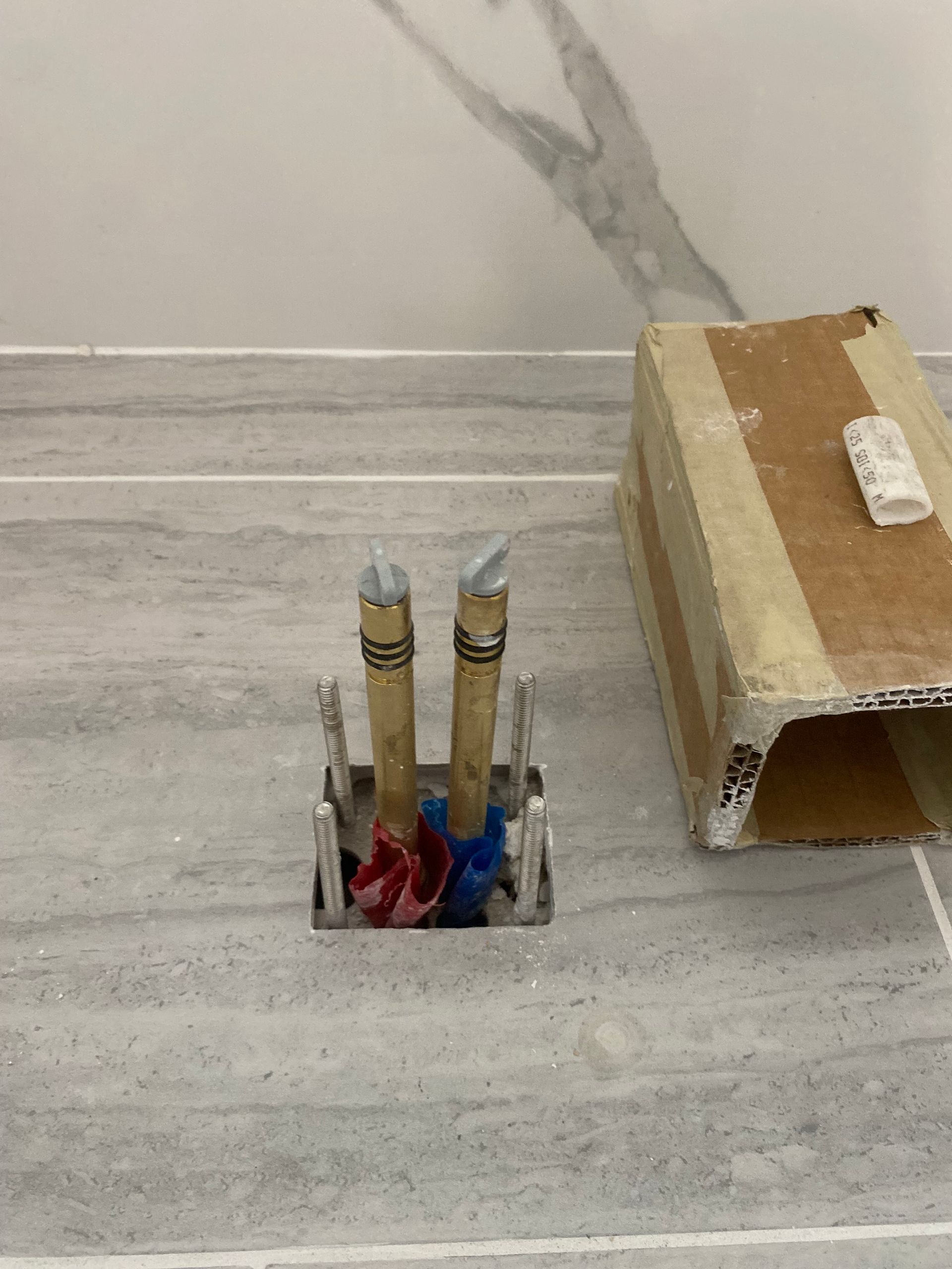 A hole in the floor with two pipes coming out of it.