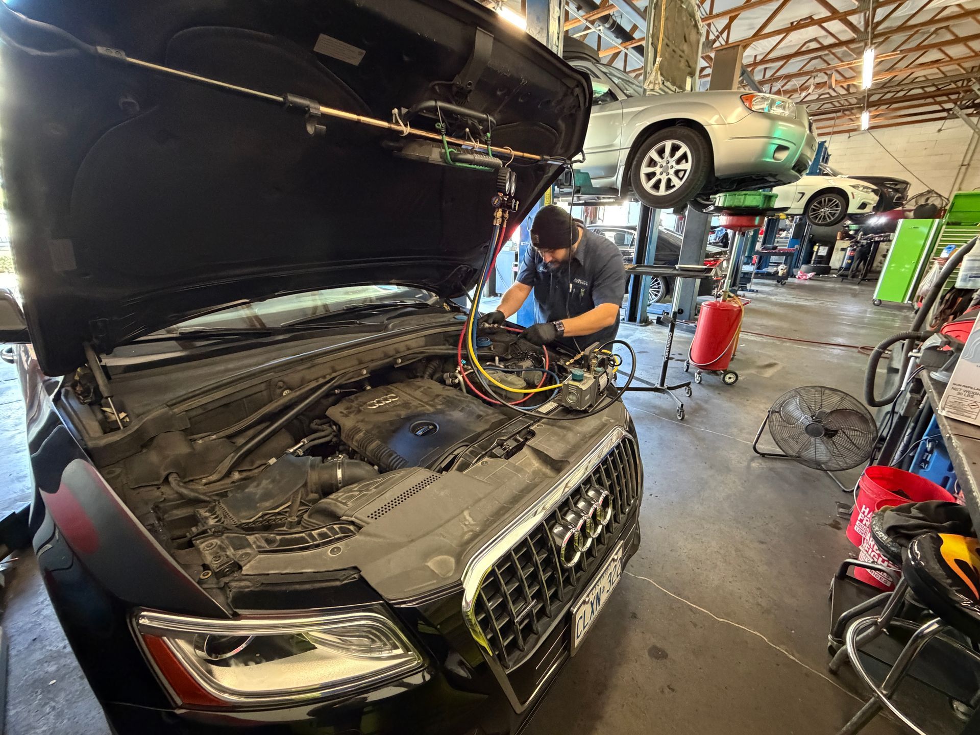Mechanic working on car engine in a garage. Other vehicles raised on lifts are visible.