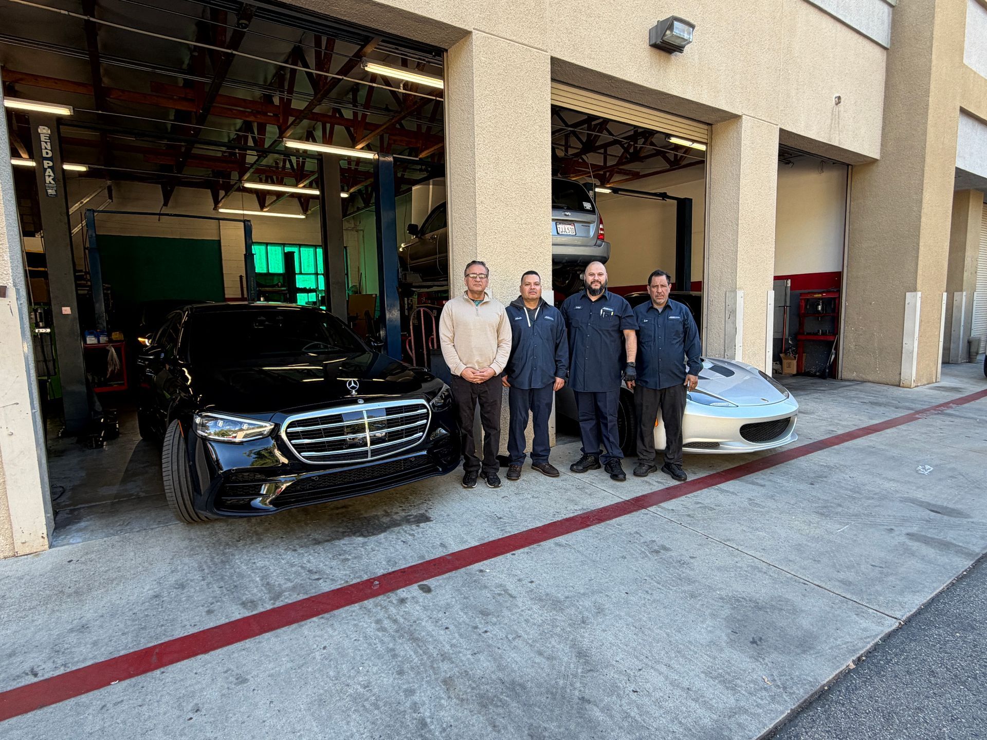 Mechanic in blue jumpsuit shows clipboard to customer in yellow shirt; car on lift.