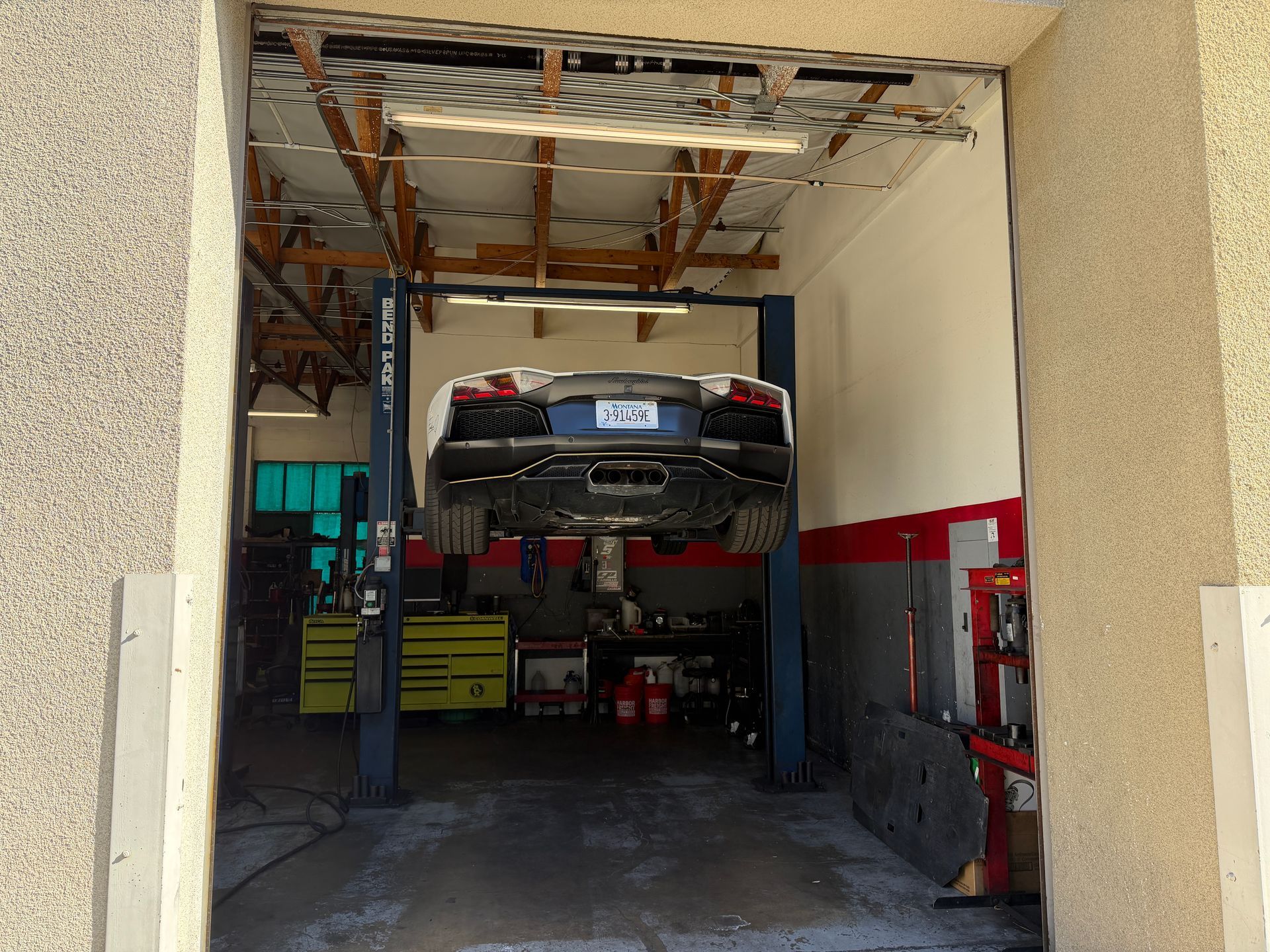 A white Lamborghini Aventador raised on a car lift inside a repair shop.