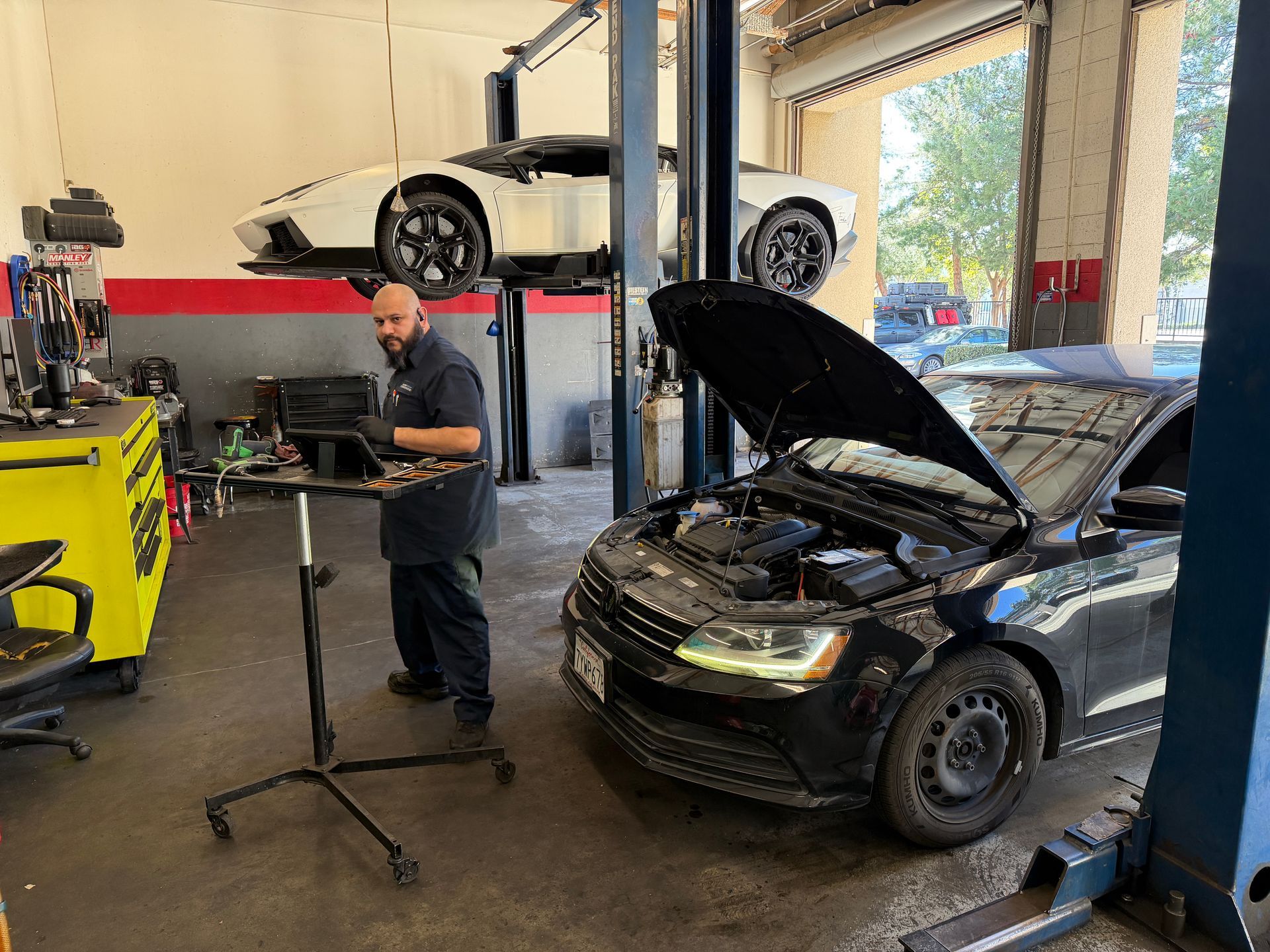 Mechanic working on a car in a shop. A white car is raised on a lift, another car's hood is open.