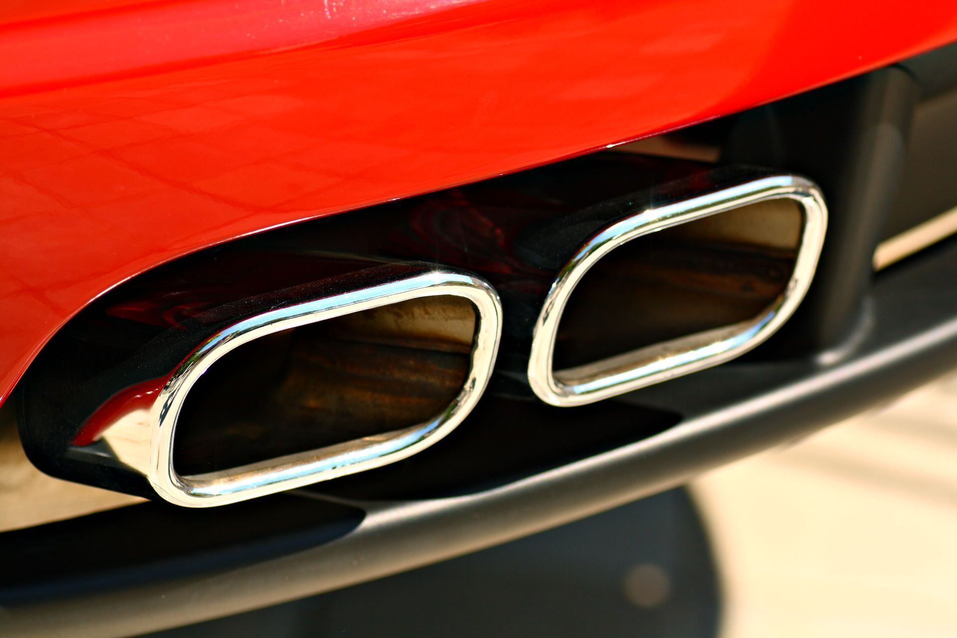 Close-up of a red car's dual chrome exhaust pipes against a black bumper.