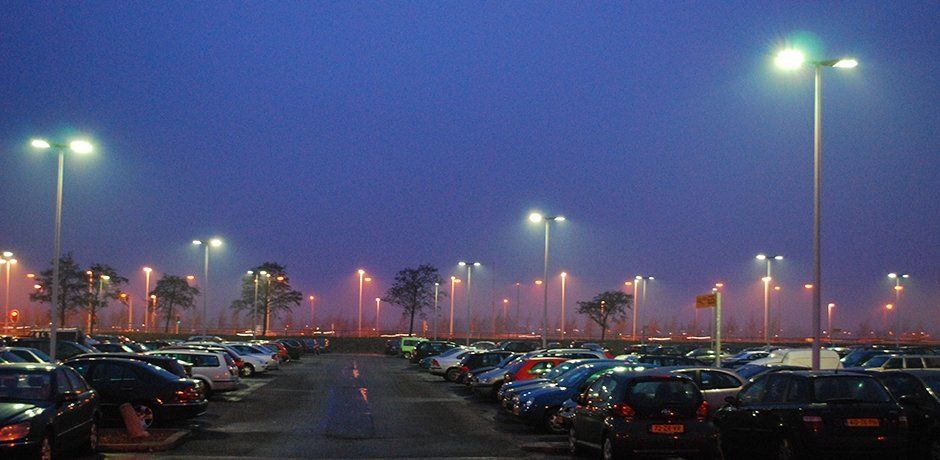 Crowded parking lot at dusk with rows of cars and tall streetlights glowing under a purple sky