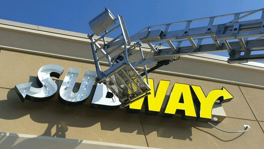 Damaged Subway storefront sign with a ladder hanging over the yellow logo