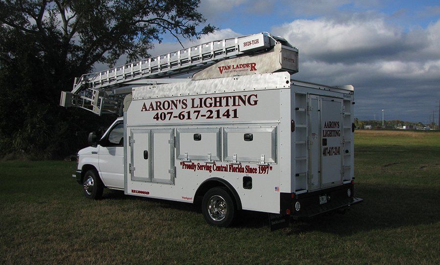 White Aaron’s Lighting service truck with ladder parked on grass in a rural field