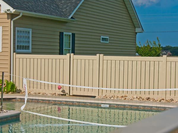 Backyard pool with white fence and beige house in the background