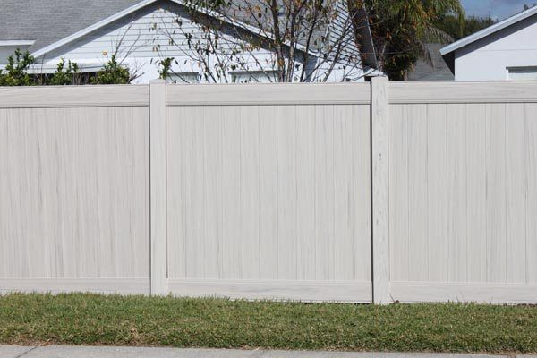 White vinyl privacy fence along a suburban yard with grass in front and houses behind