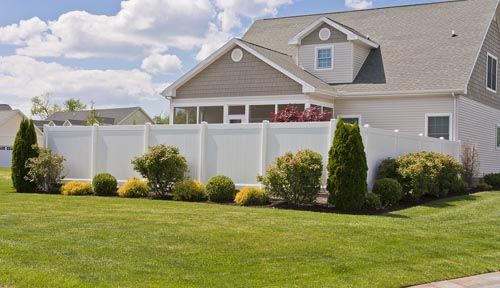 Suburban house with white fence, green lawn, and trimmed shrubs under a cloudy sky