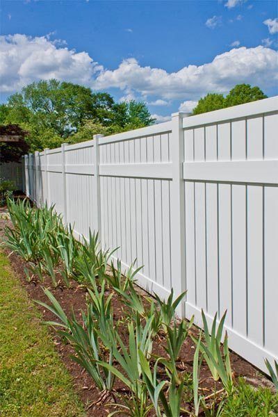White vinyl fence beside a narrow garden bed of green plants under a blue sky