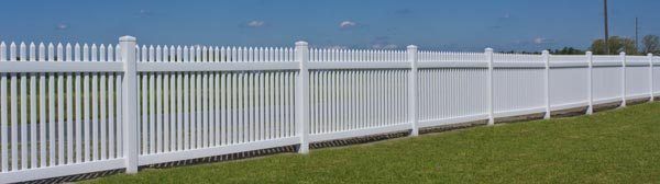 White picket fence along a grassy field under a clear blue sky