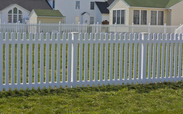 White picket fence in front of suburban houses and green grass.