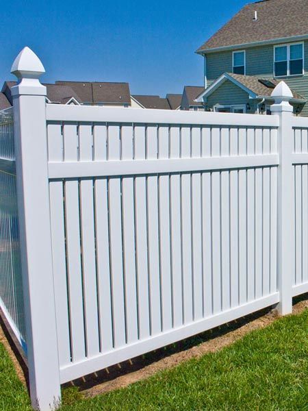 White vinyl privacy fence along a residential yard under a blue sky.