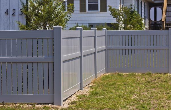 Light gray vinyl fence beside a grassy yard in front of a house.
